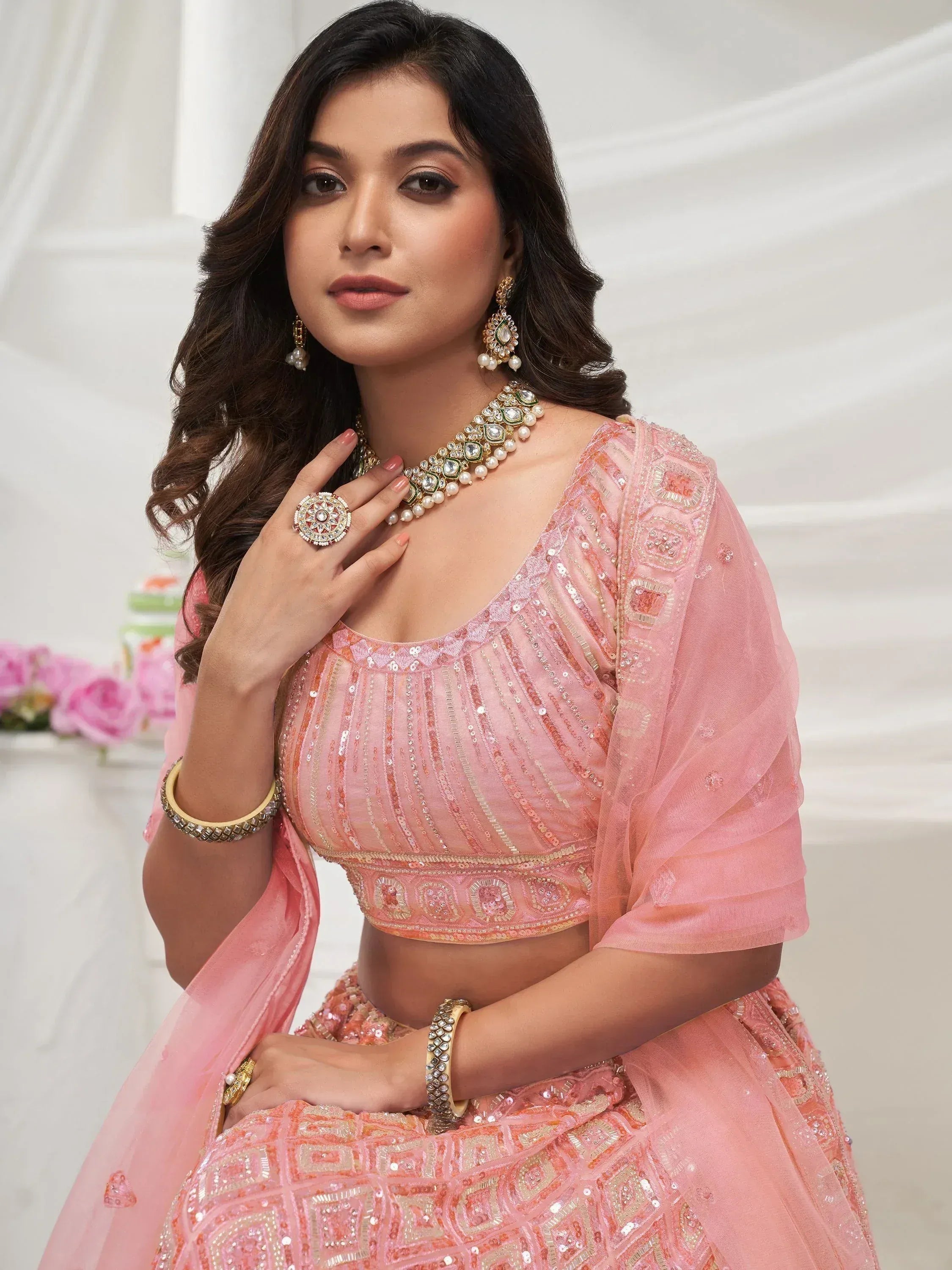Pink embroidered lehenga choli with sequins, paired with traditional Indian jewelry for festive occasions