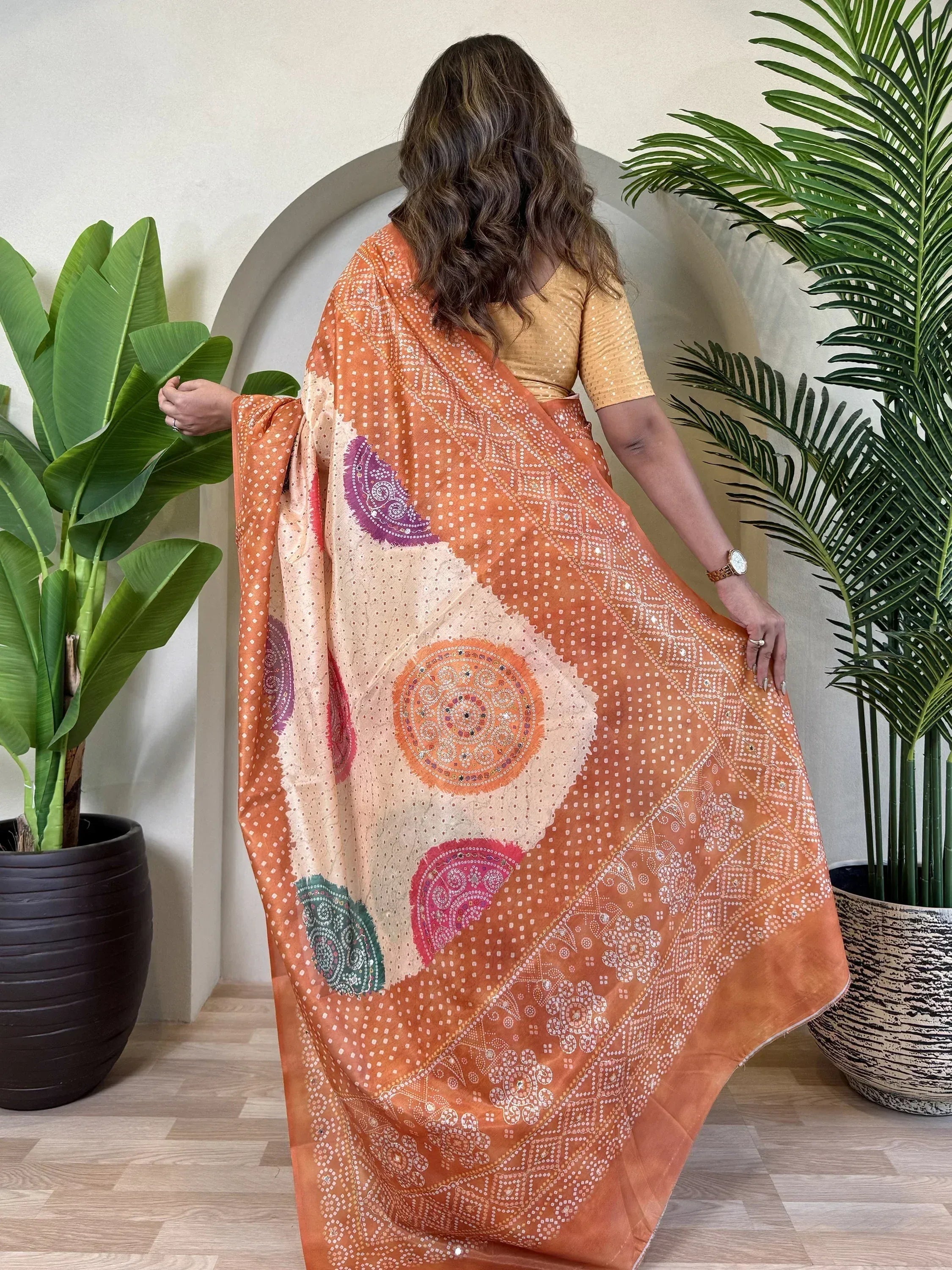 Woman wearing orange printed saree with mirror work and paisley motifs, styled with yellow blouse