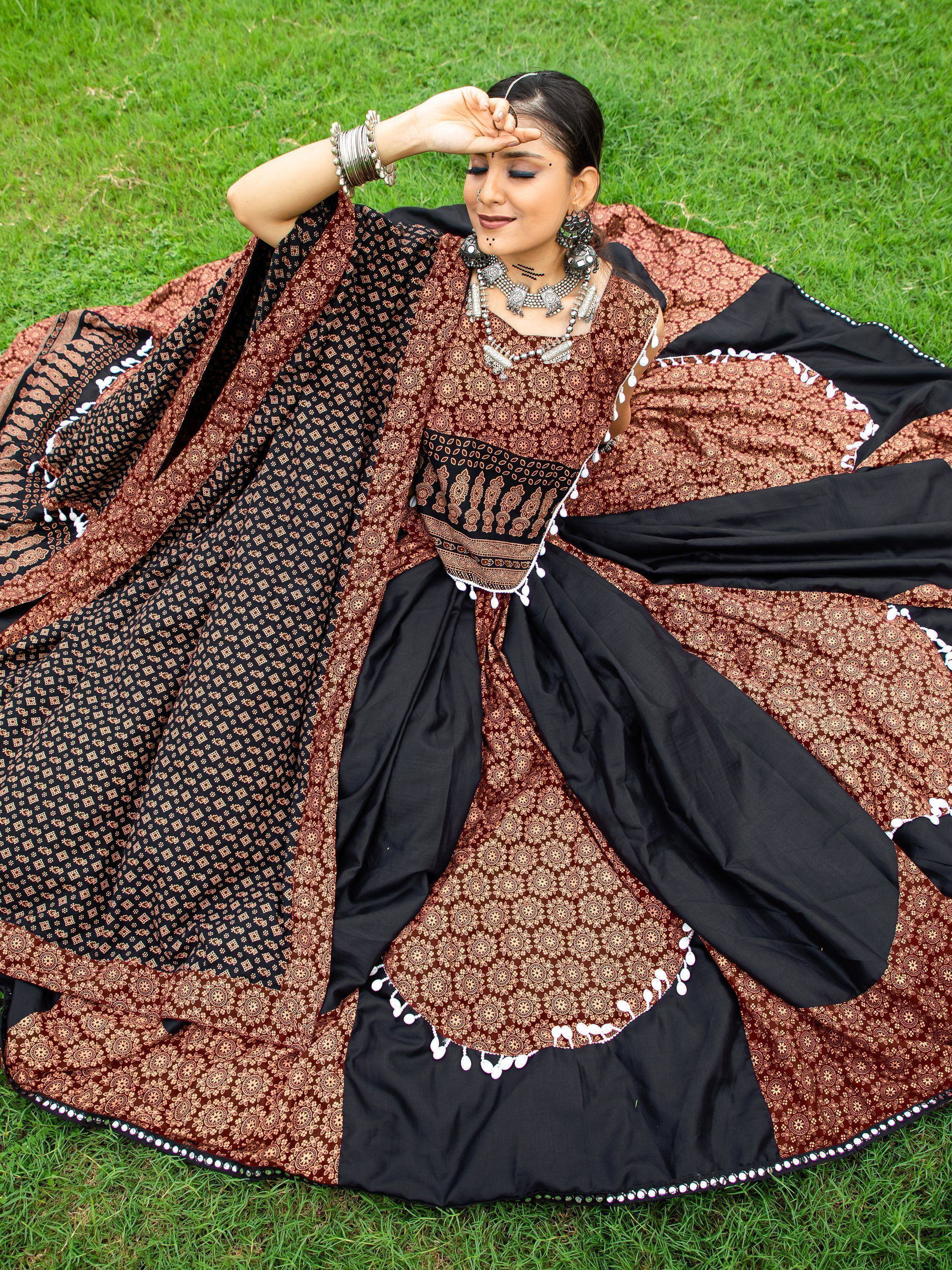 Woman in elegant black and maroon printed ethnic gown with mirror work, lying on grass