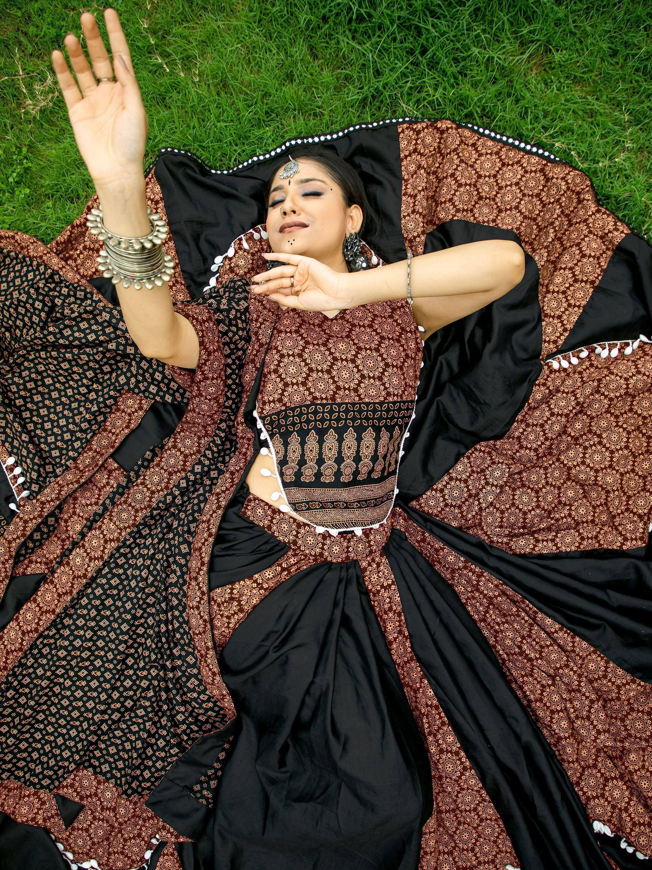 Woman in black and brown printed lehenga choli lying on grass, ethnic Indian wear with silver jewelry