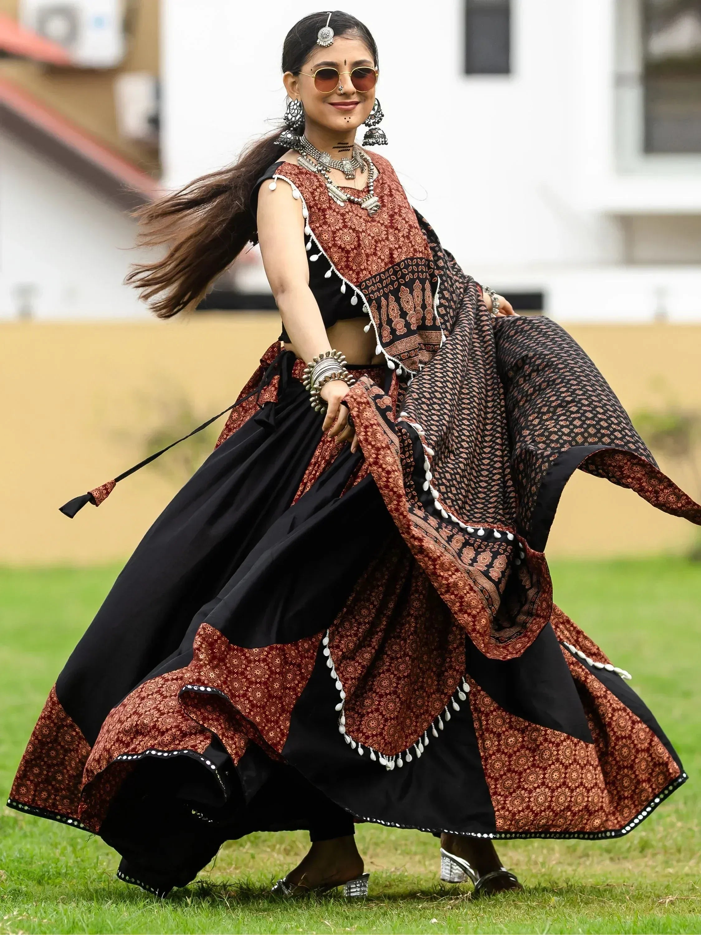 Woman in black and maroon printed lehenga choli with silver jewelry, dancing outdoors