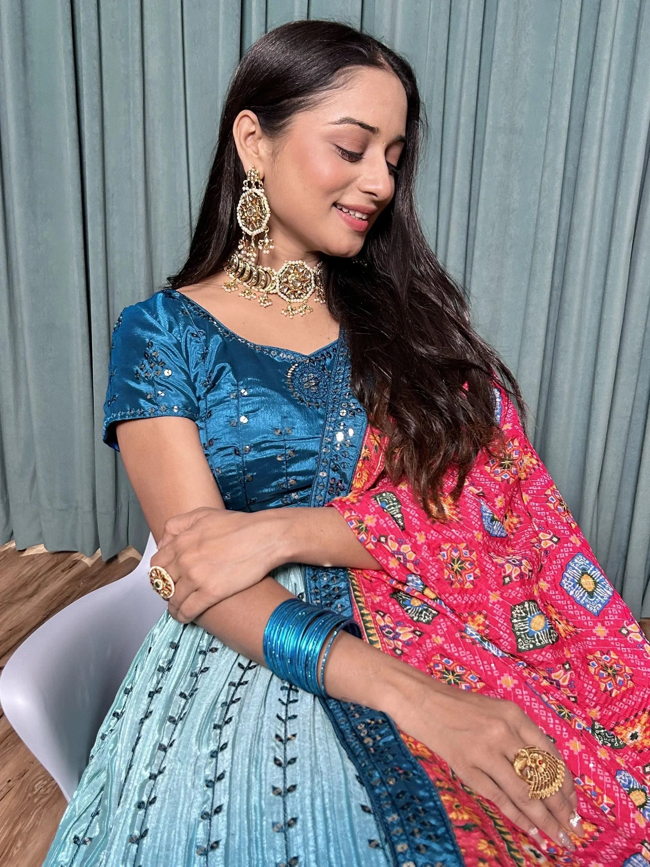 Woman in blue embroidered lehenga choli with pink printed dupatta, gold jewelry, and bangles