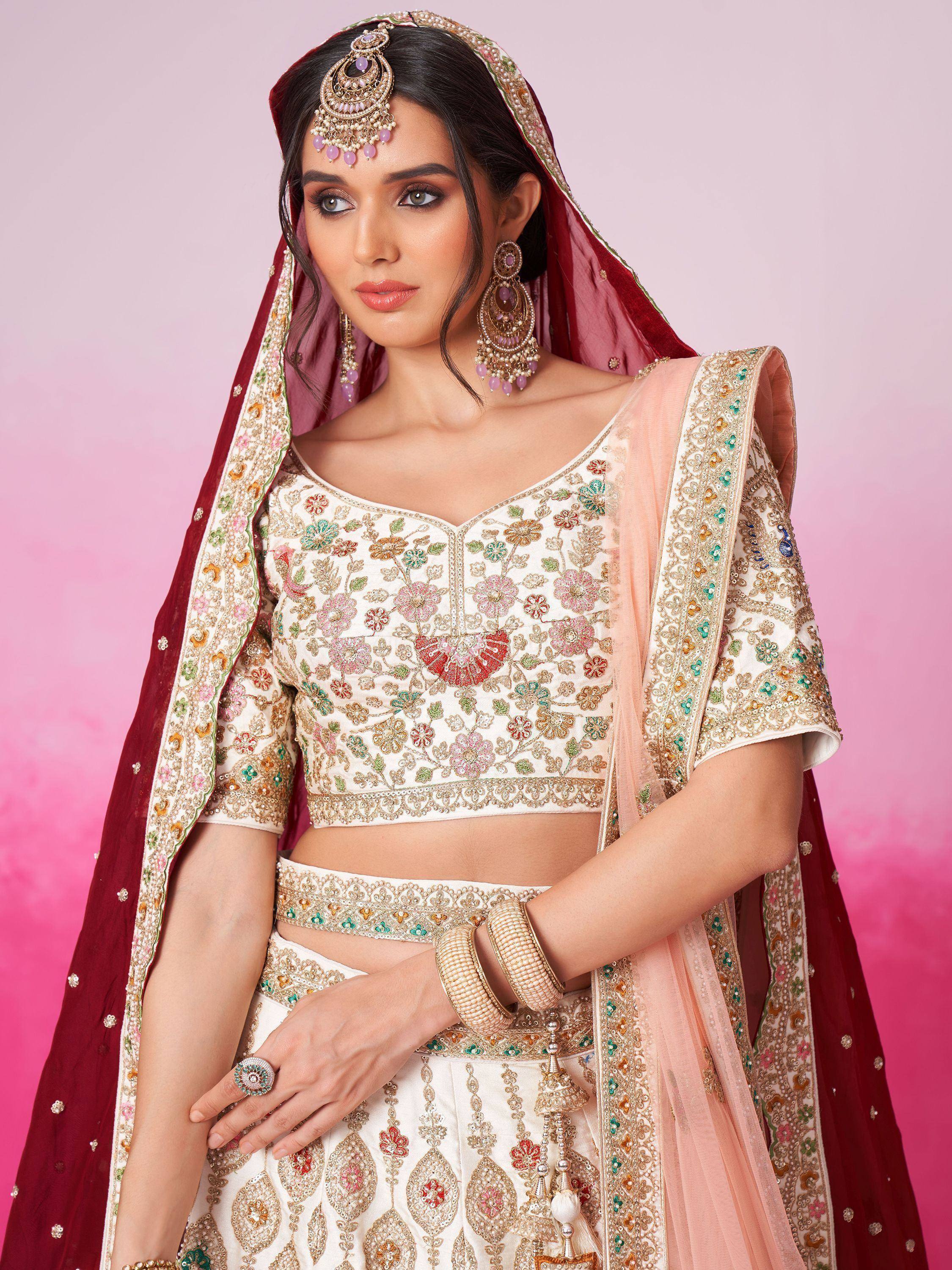 Elegant ivory lehenga choli with floral embroidery, paired with maroon dupatta and traditional jewelry for Indian weddings.