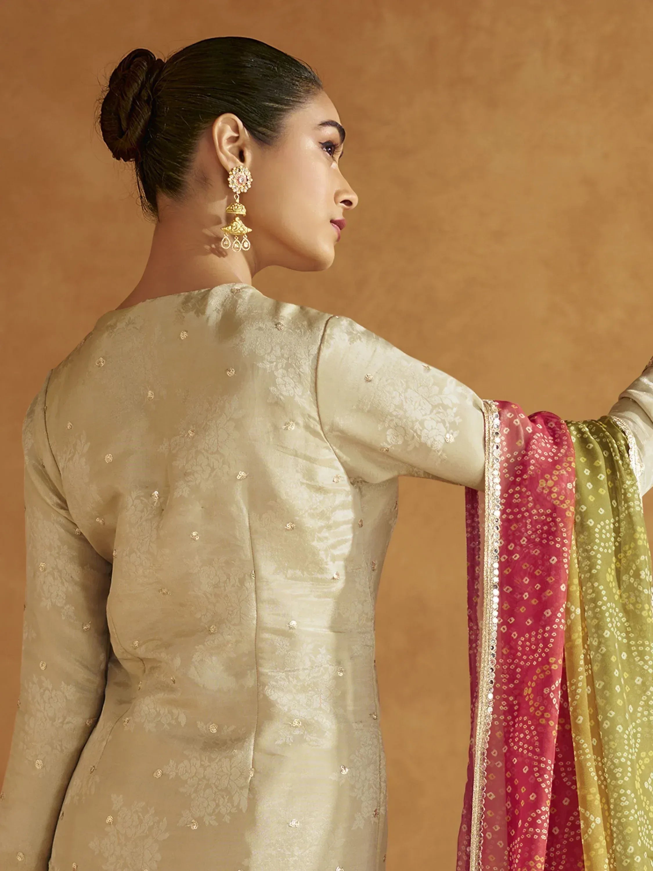 Woman in elegant beige embroidered salwar kameez with pink and green dupatta, showcasing traditional Indian ethnic wear.