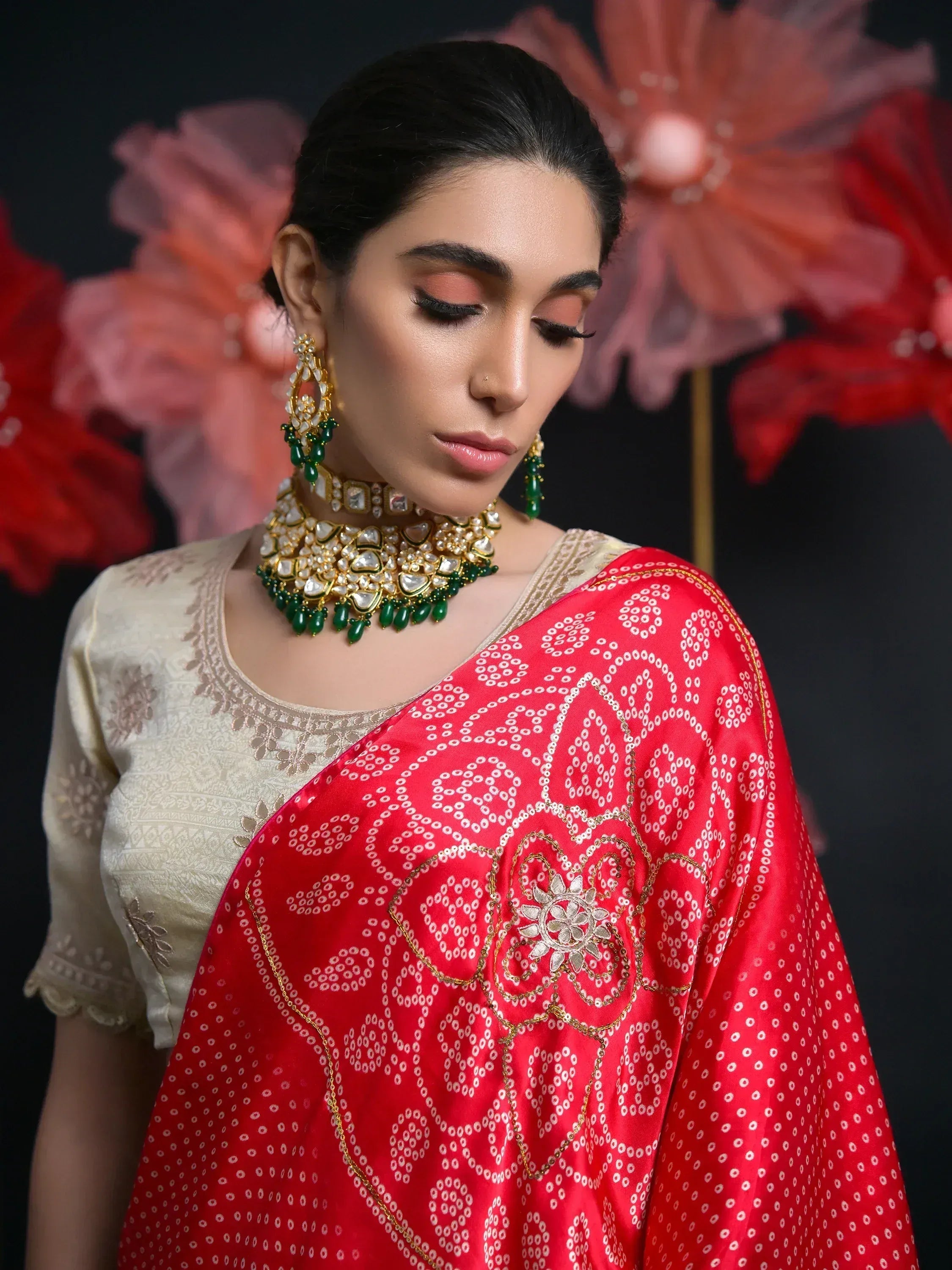 Woman in red printed saree with gold embroidery, cream blouse, and green gold jewelry