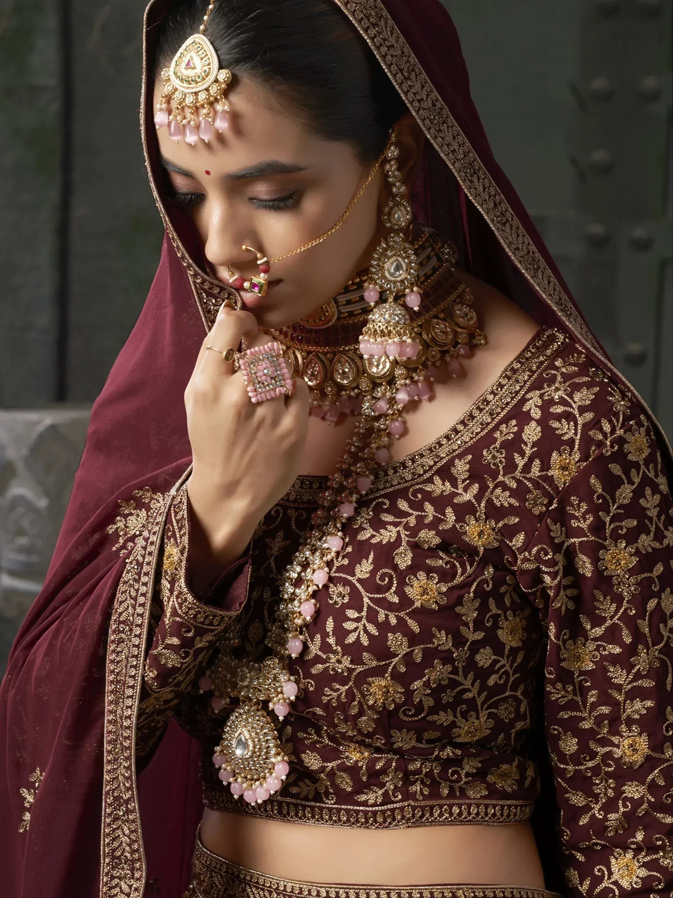 Maroon embroidered lehenga choli with gold detailing and pink stone jewelry for Indian ethnic wear