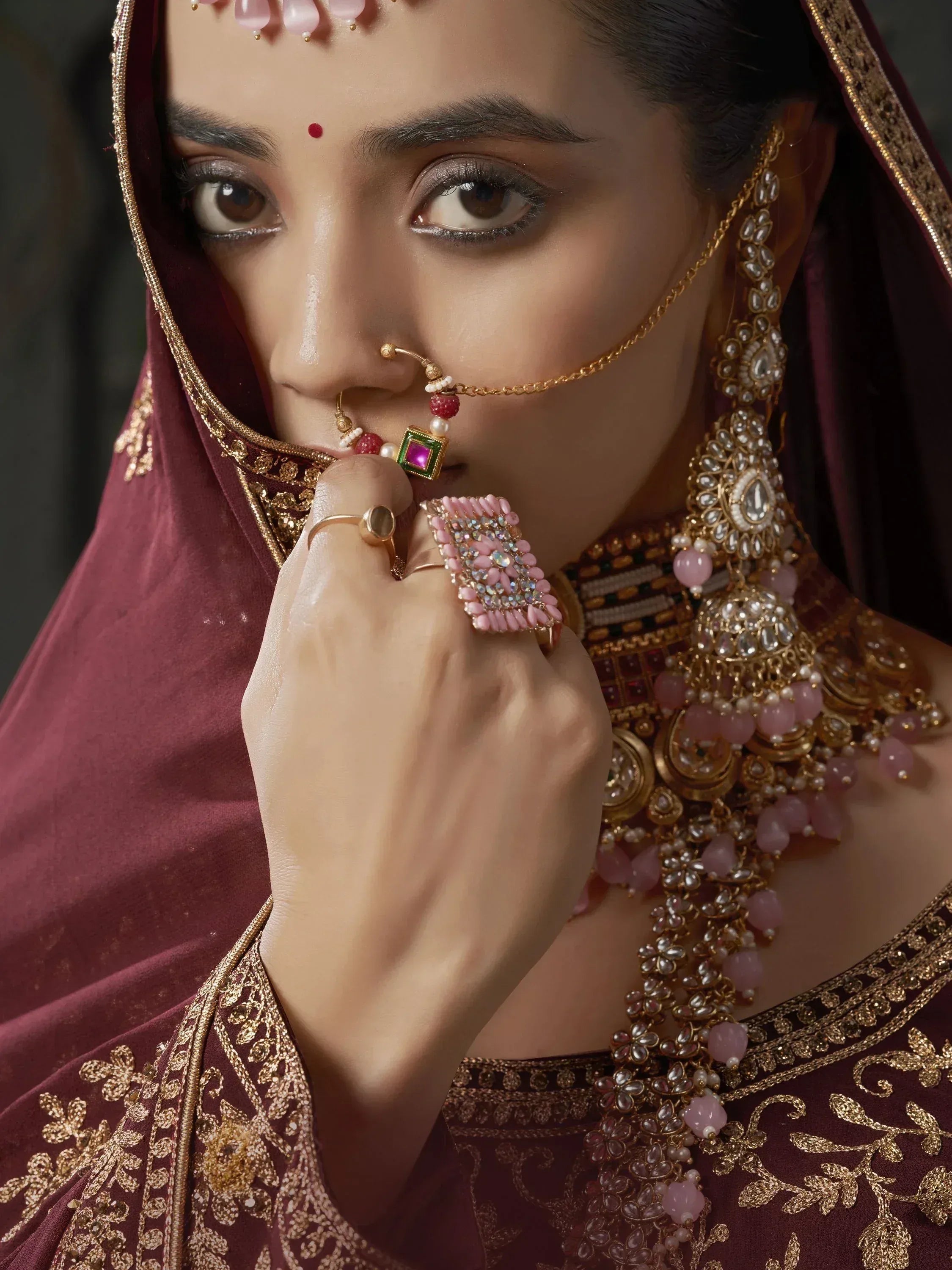 Bridal Indian ethnic wear with maroon lehenga, gold embroidery, and pink gemstone jewelry