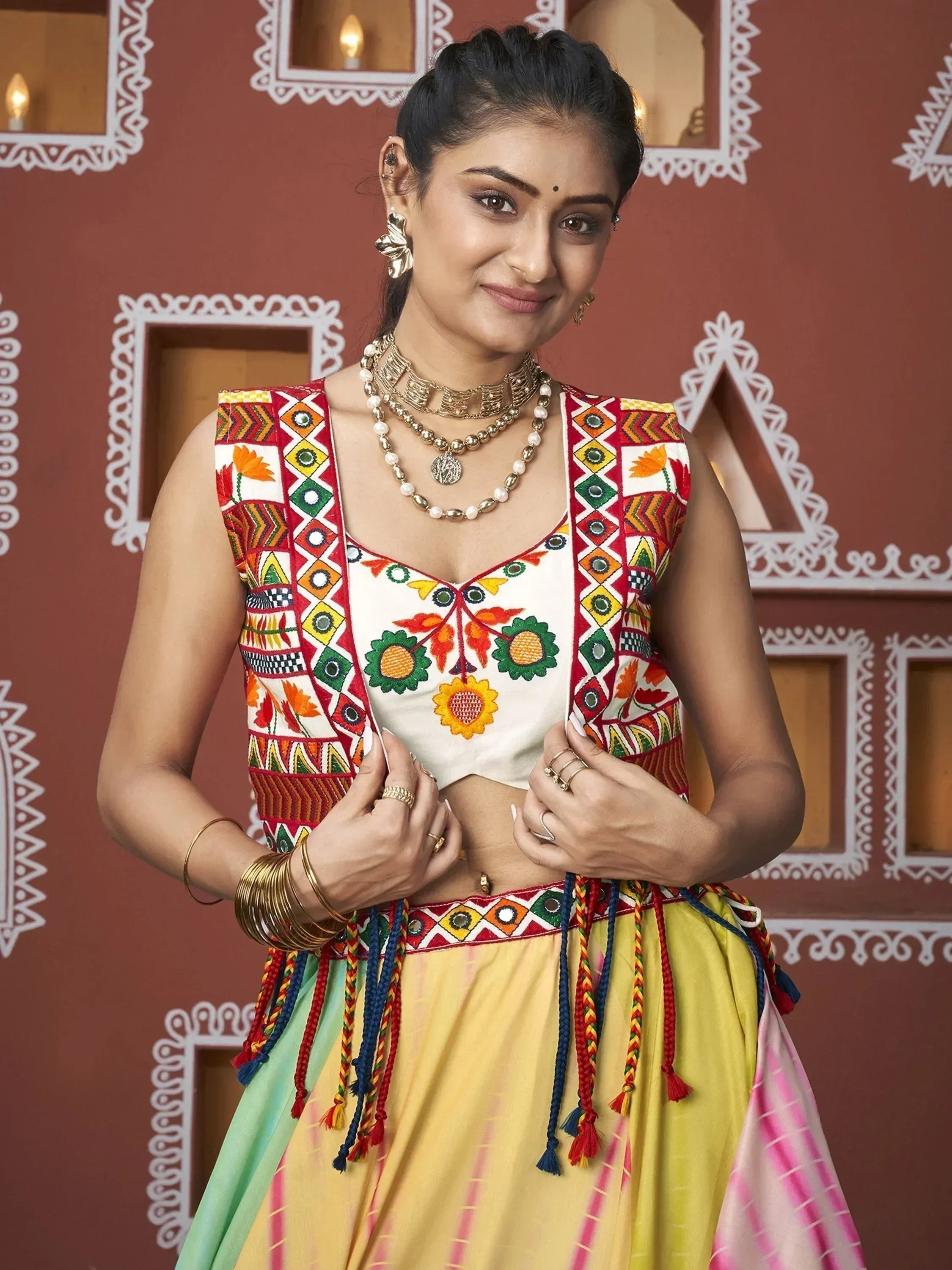 Woman in colorful embroidered Indian ethnic wear with floral patterns and tassels, styled with gold jewelry.
