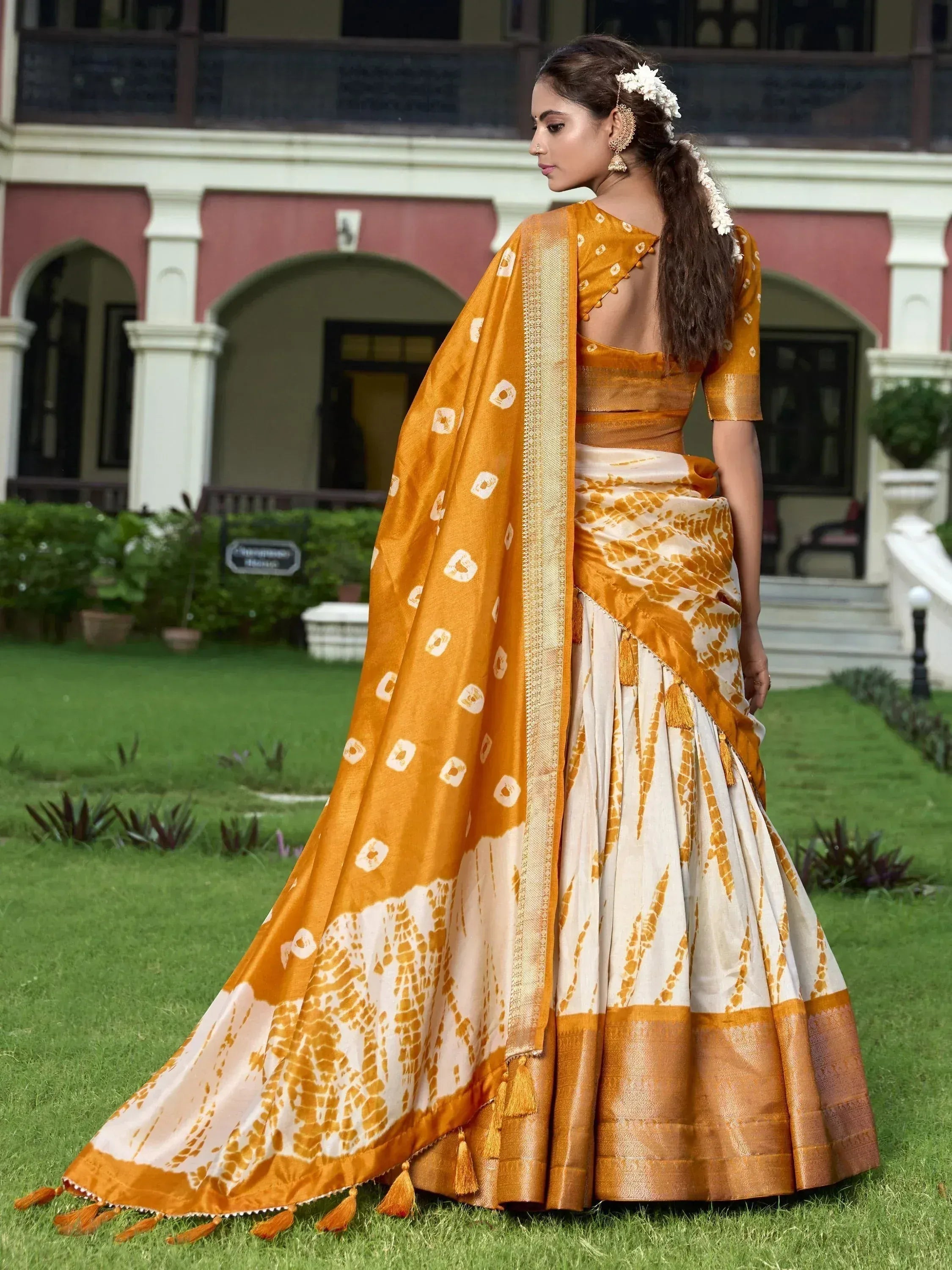Woman in mustard and cream printed lehenga choli with gold border, floral hair accessory, garden setting