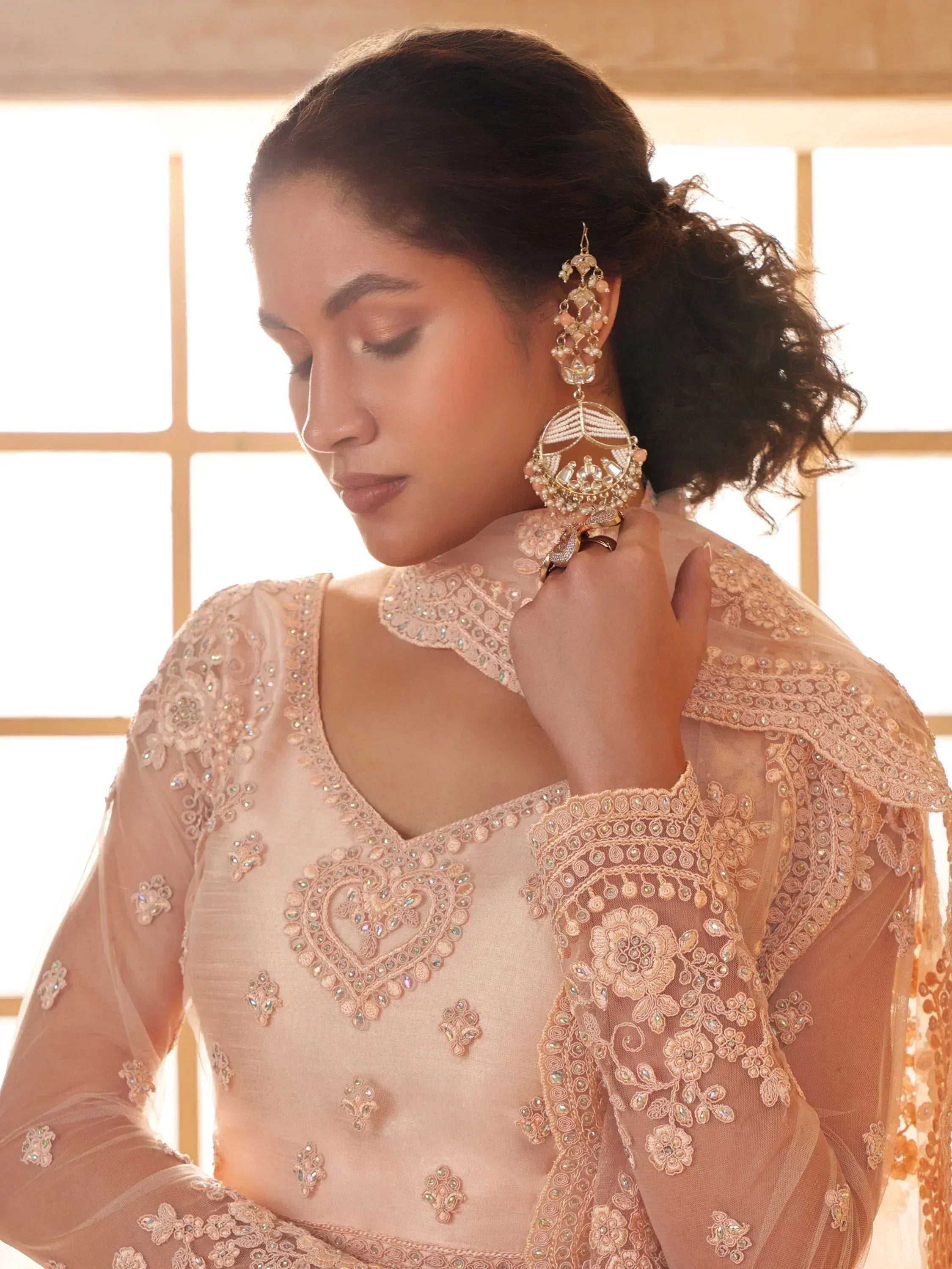Elegant peach ethnic gown with floral embroidery and statement jhumka earrings for Indian occasions