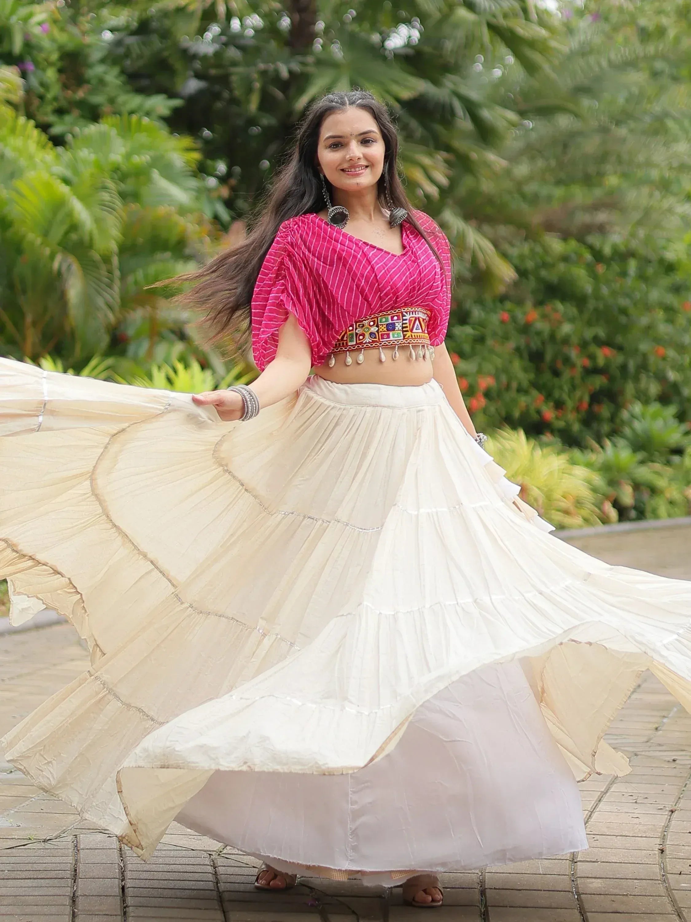 Woman twirling in pink embroidered crop top and flowing white tiered skirt, Indian ethnic wear