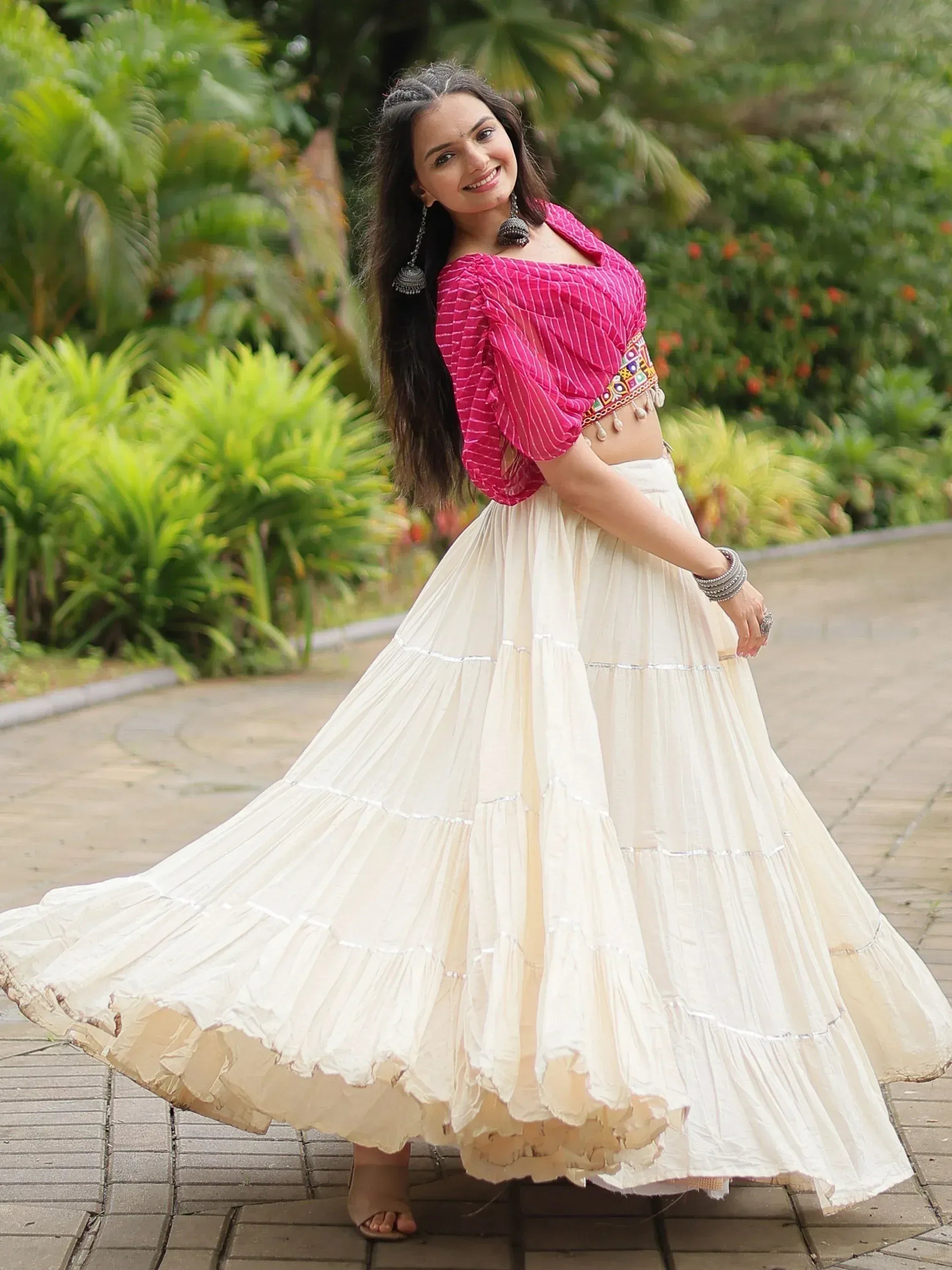 Woman in pink striped crop top and cream tiered skirt, ethnic Indian wear, garden setting