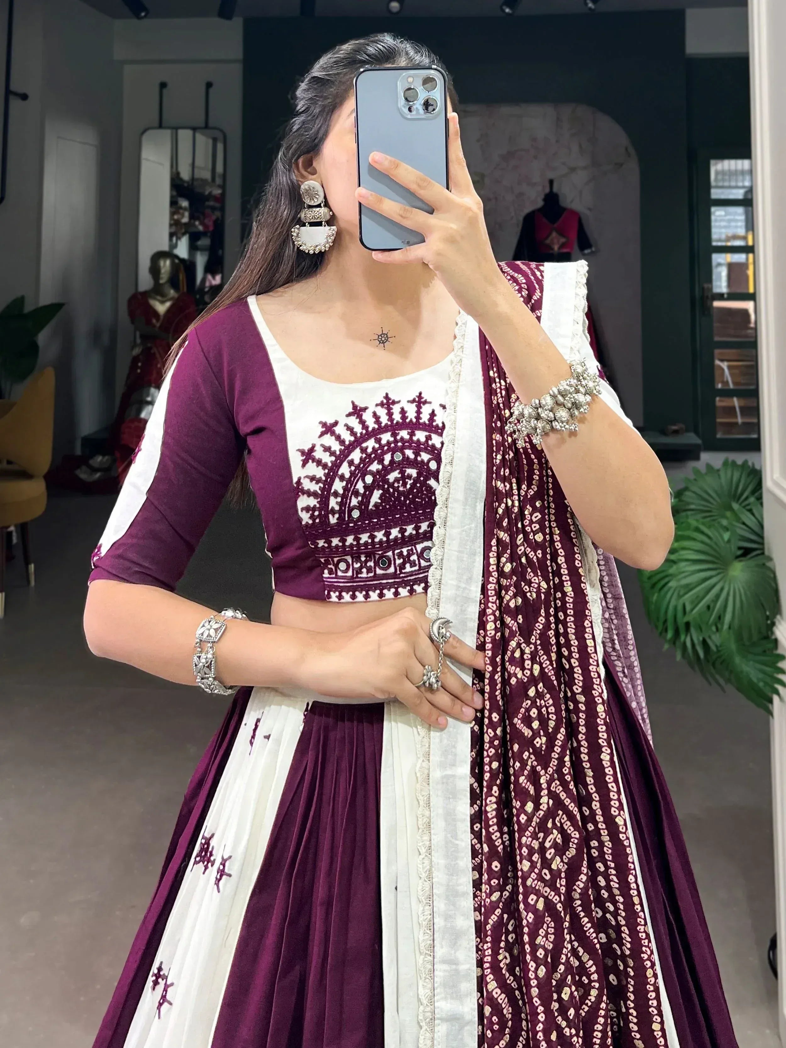 Woman in maroon and white embroidered lehenga choli with mirror work, taking mirror selfie in boutique