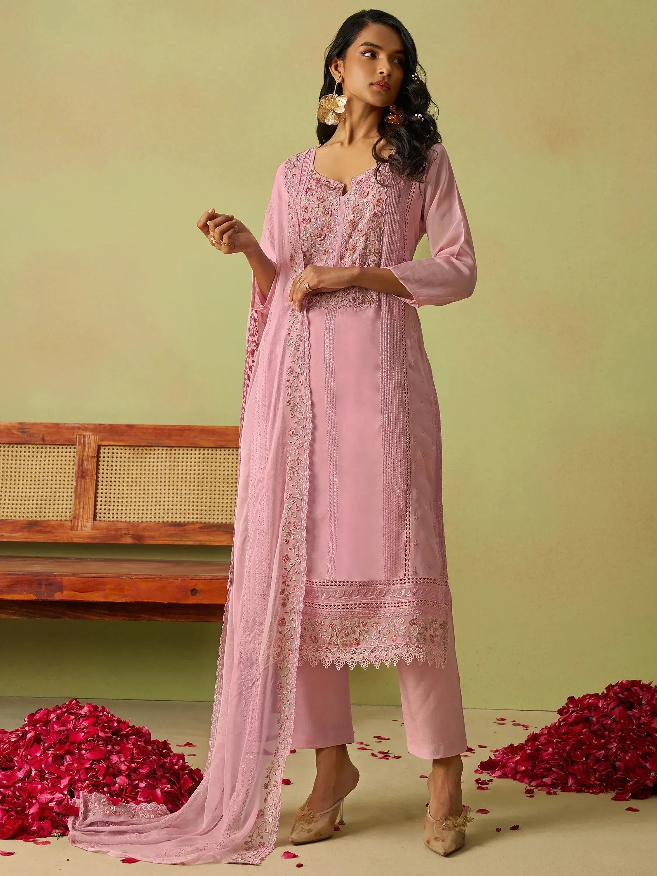 Pink embroidered salwar kameez with matching dupatta, floral detailing, and rose petals on floor