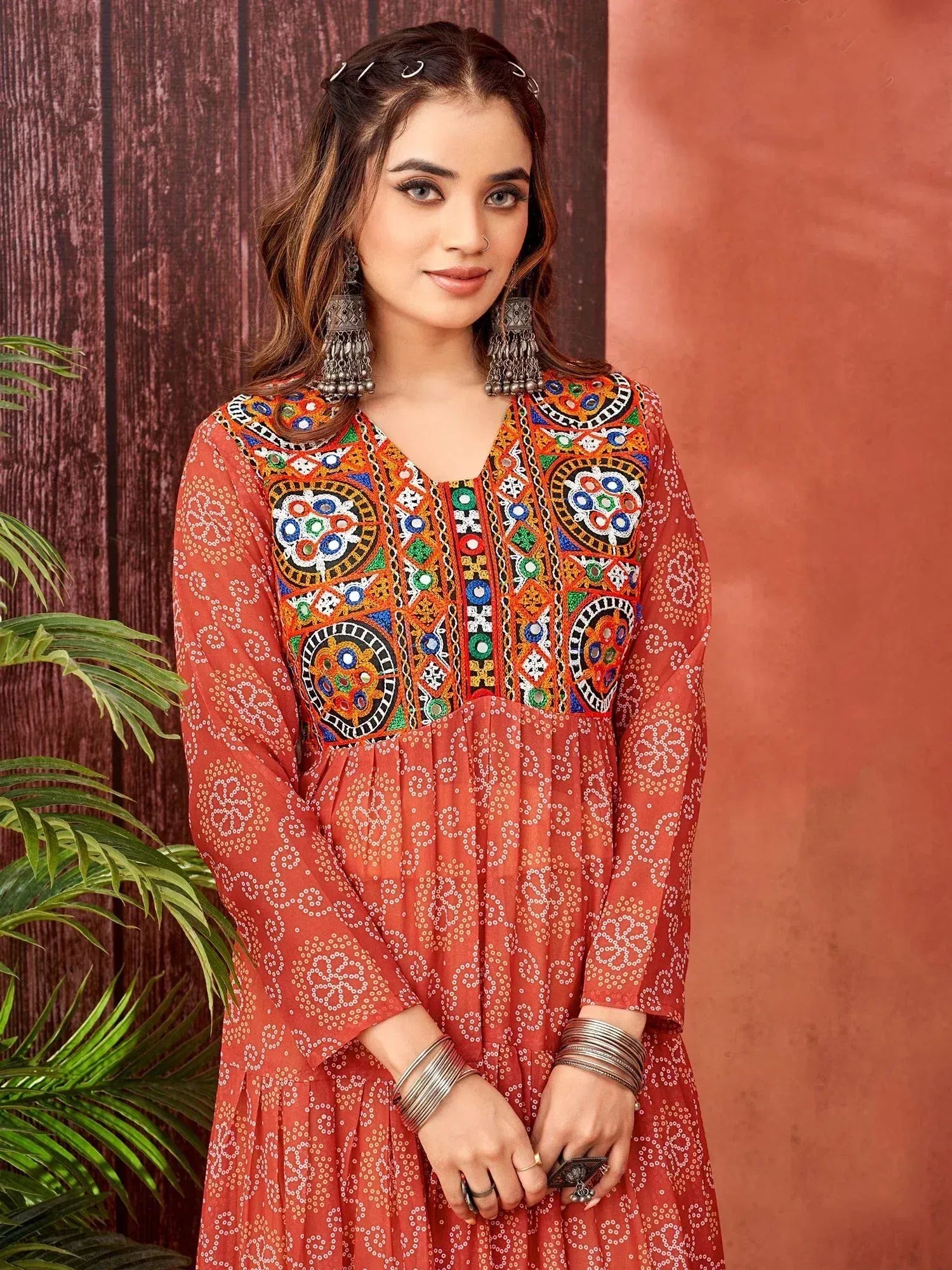 Woman in vibrant orange ethnic kurti with colorful mirror embroidery and white bandhani print, styled with jhumka earrings.