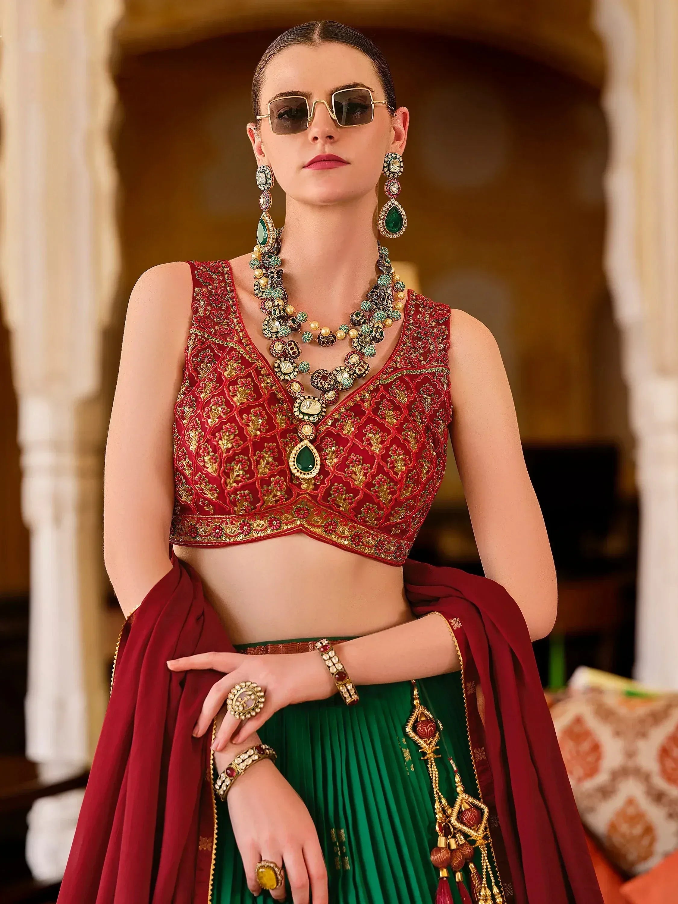 Red and green embroidered lehenga choli with heavy jewelry and sunglasses