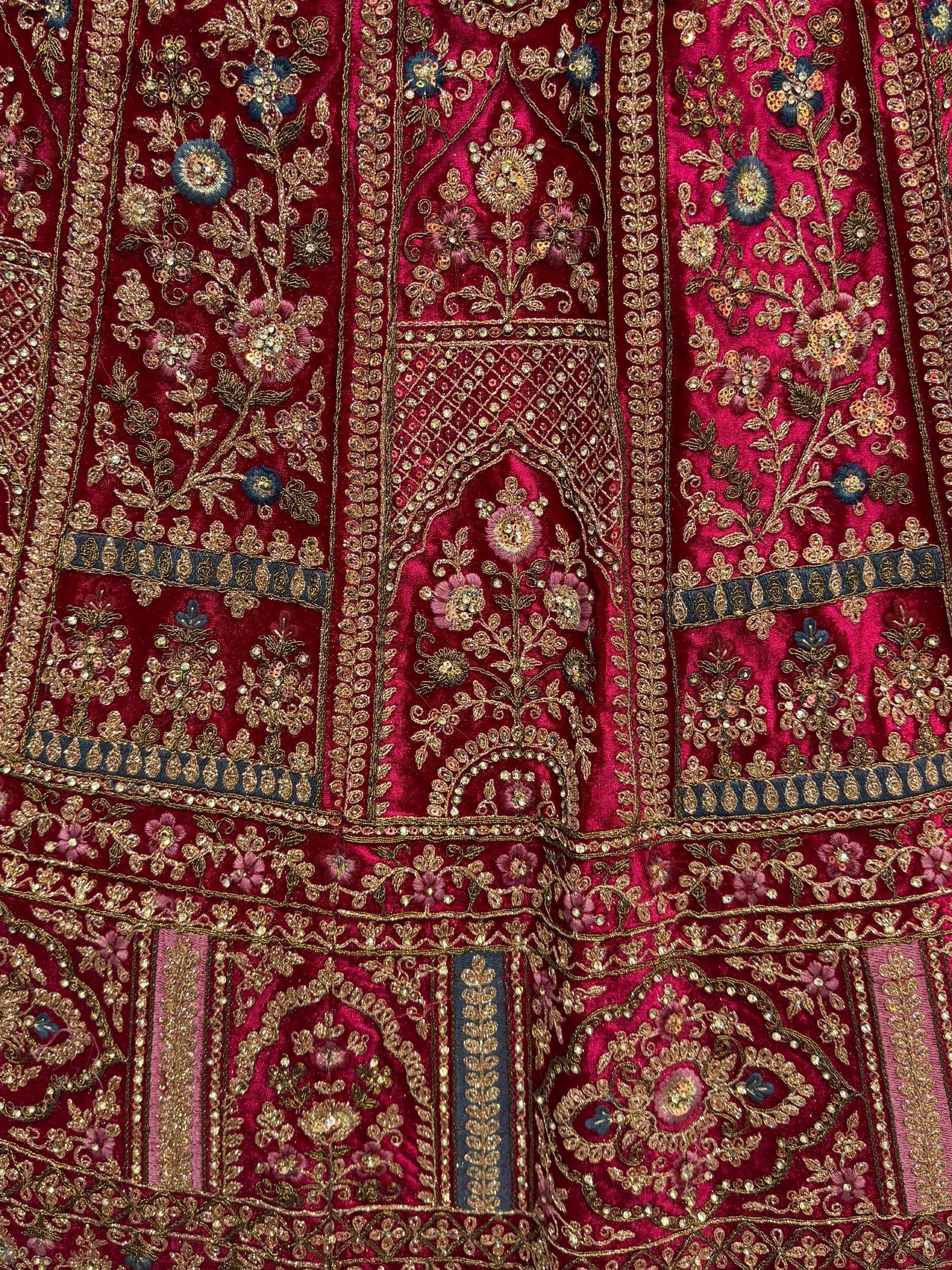 Richly embroidered Indian ethnic wear with gold floral motifs and sequins on deep red velvet fabric.