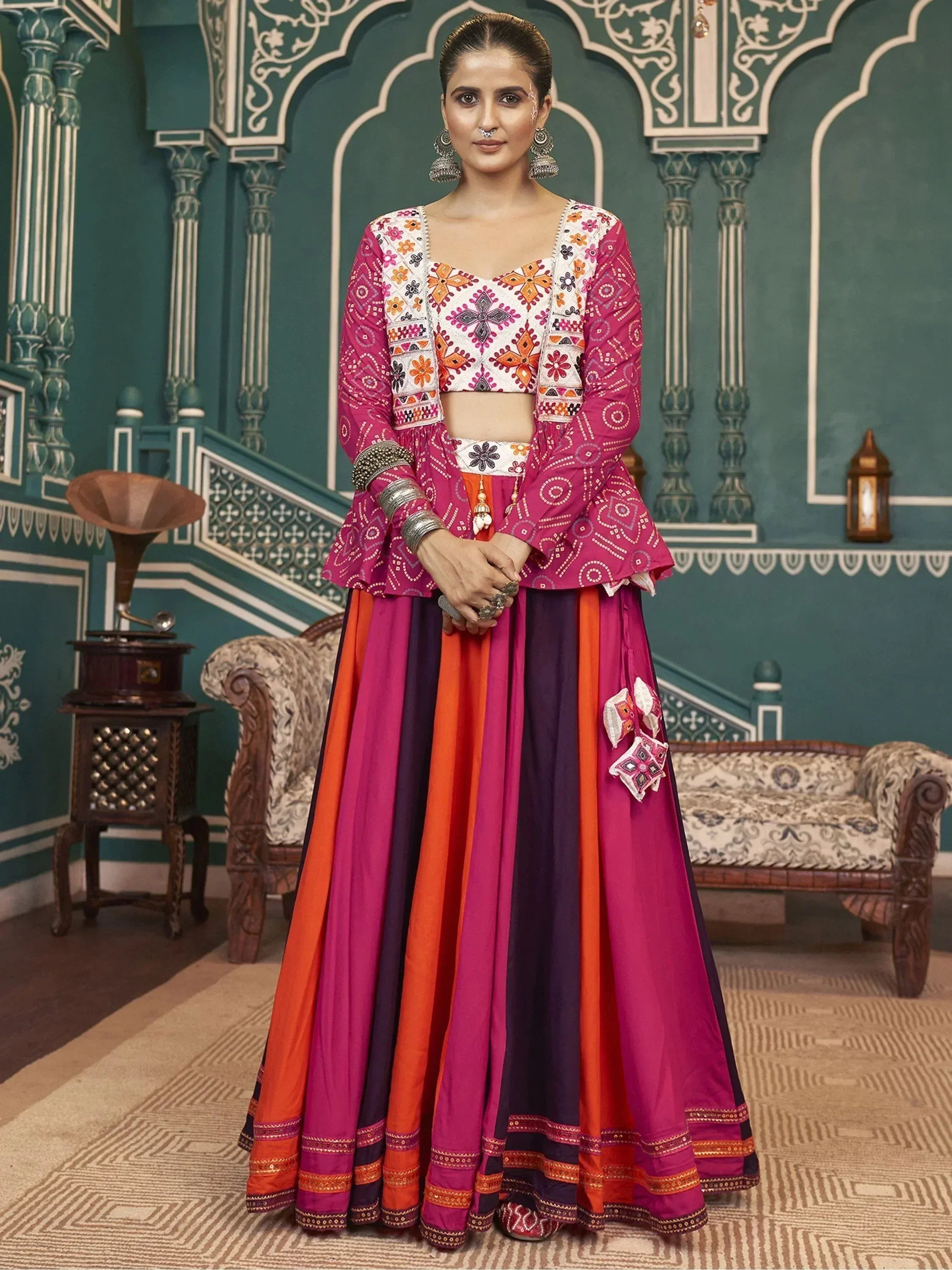 Woman in vibrant pink and orange embroidered lehenga choli with traditional Indian motifs, perfect for festive occasions.