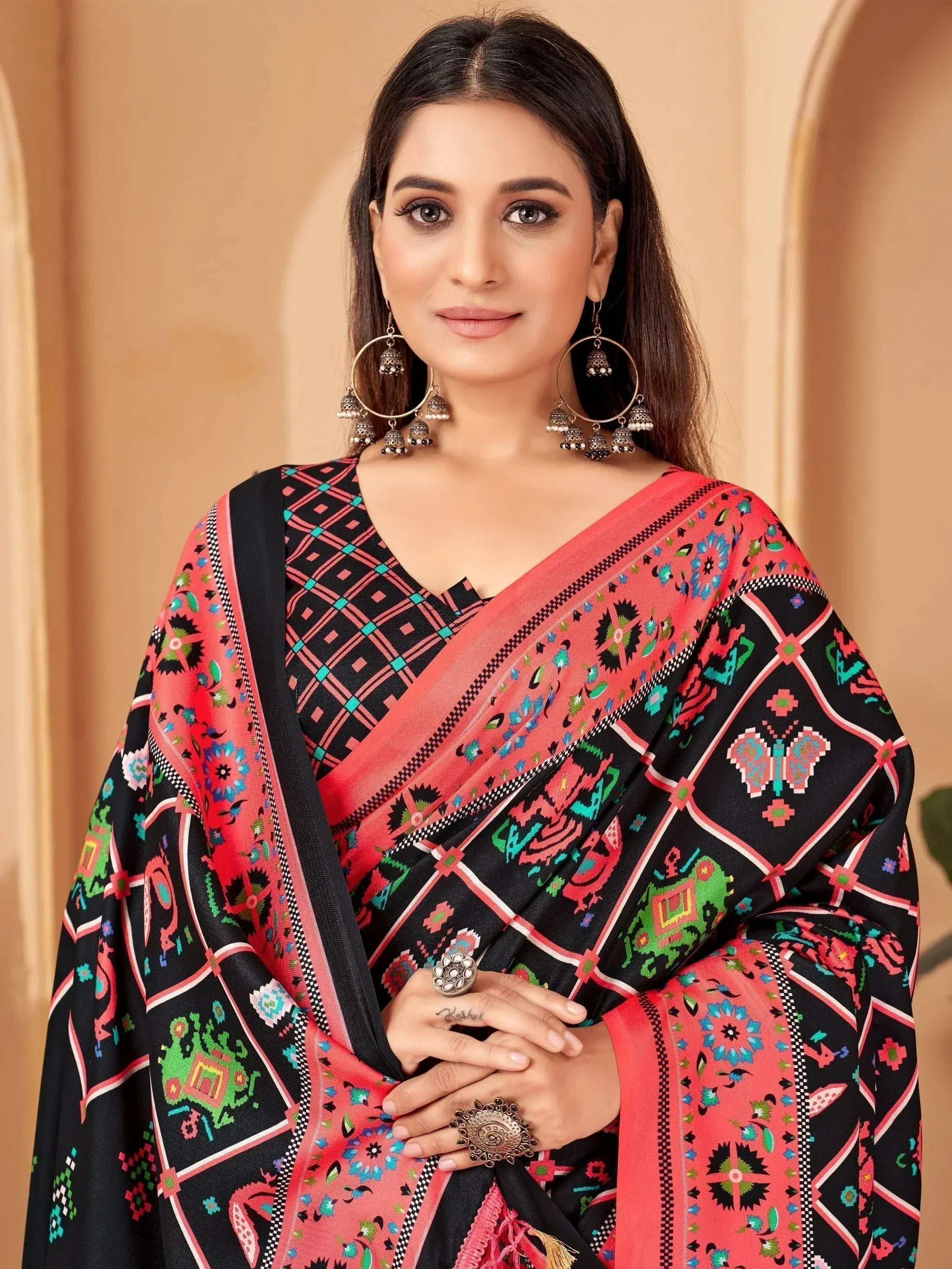 Woman in black and coral printed saree with ethnic motifs, jhumka earrings, and statement rings
