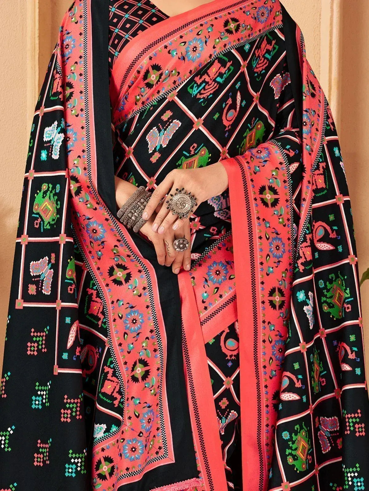 Black and coral ethnic saree with vibrant folk print and embroidered border, styled with traditional jewelry
