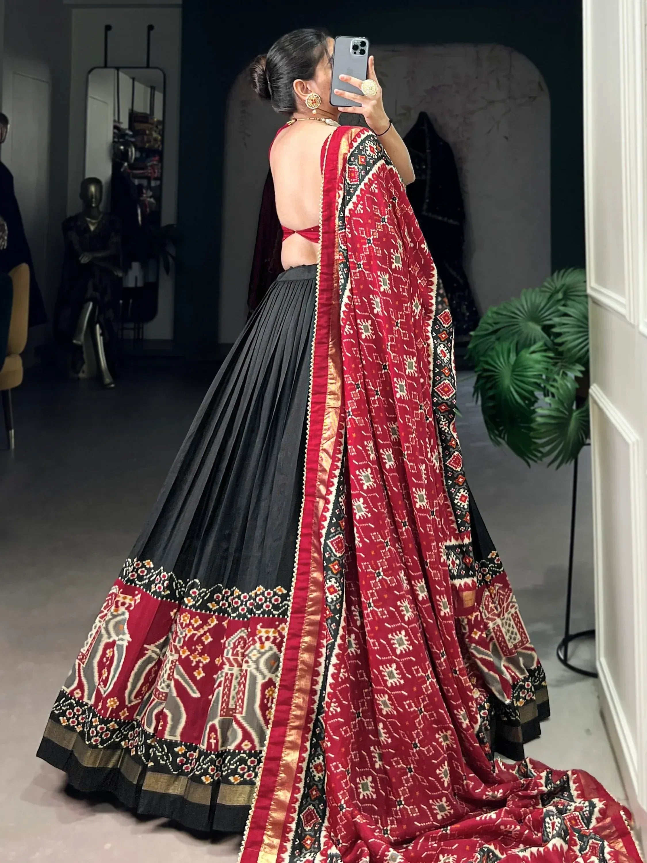 Woman in black and red printed lehenga choli with backless blouse, taking mirror selfie in boutique