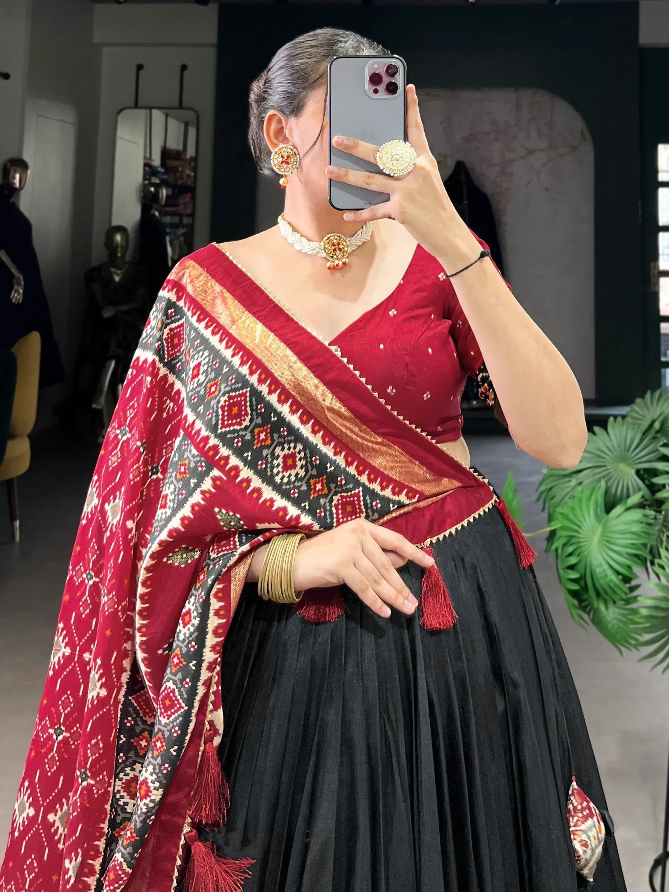 Woman in red and black ethnic lehenga choli with patterned dupatta, traditional jewelry, taking mirror selfie