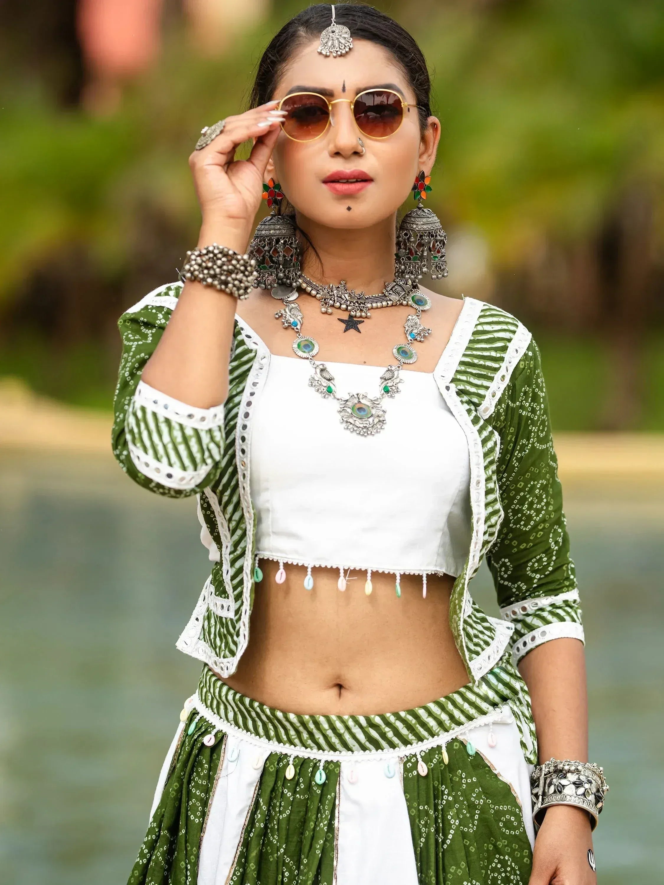 Woman in green and white ethnic lehenga choli with silver jewelry and sunglasses, styled for festive occasions.