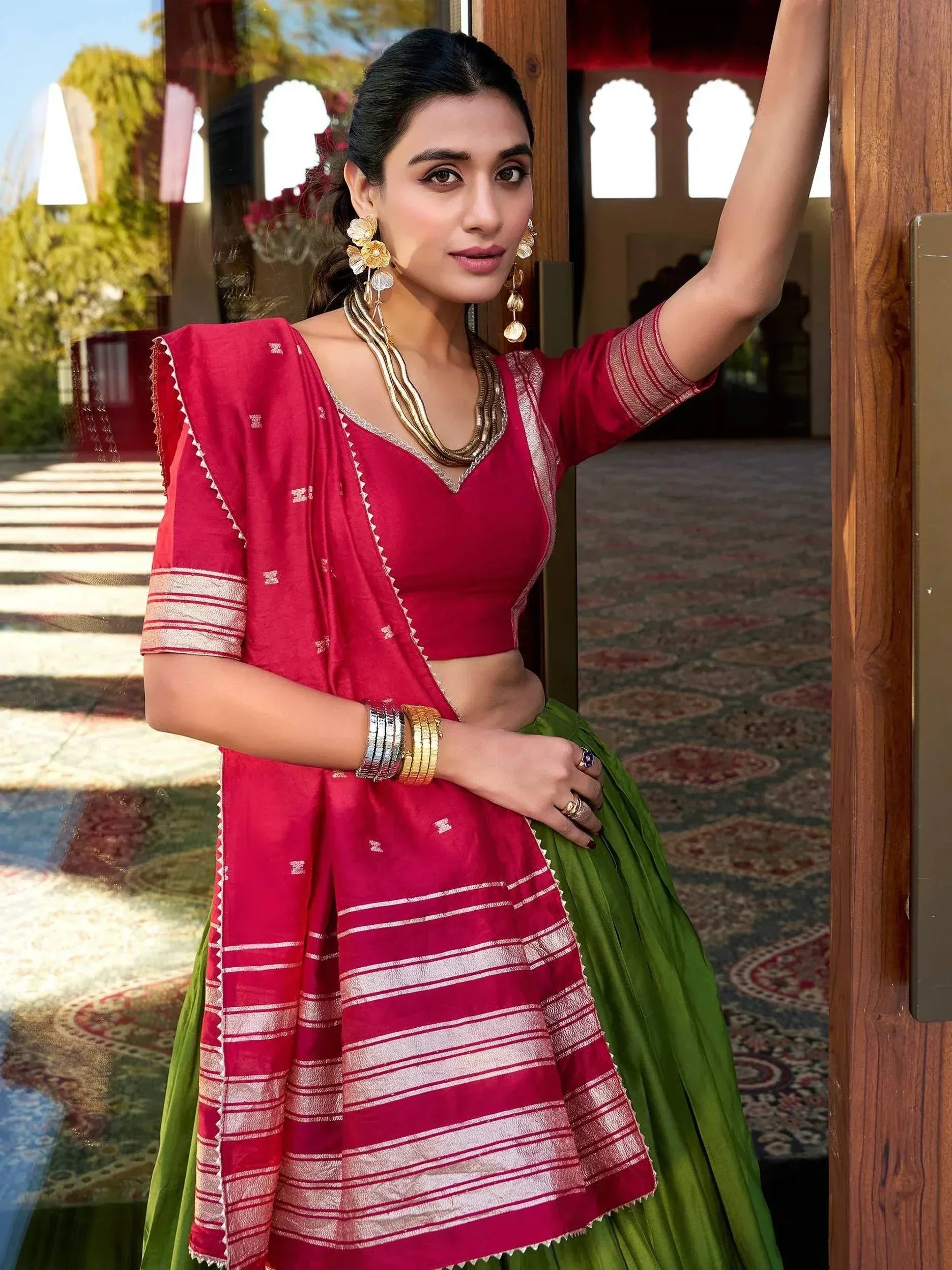 Woman in red and green ethnic lehenga choli with gold jewelry, traditional Indian attire