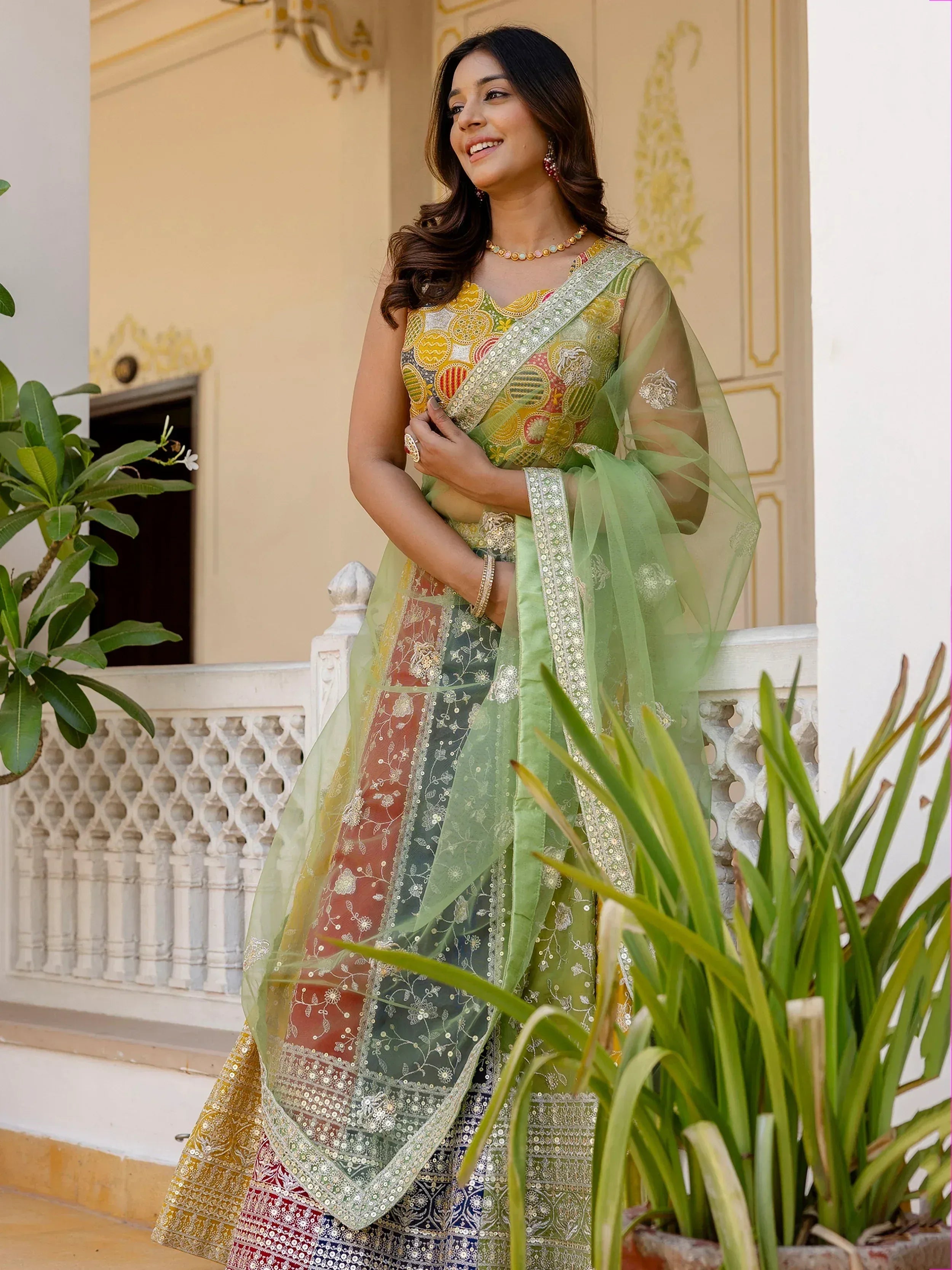 Woman in colorful embroidered Indian ethnic wear with green dupatta, standing on balcony