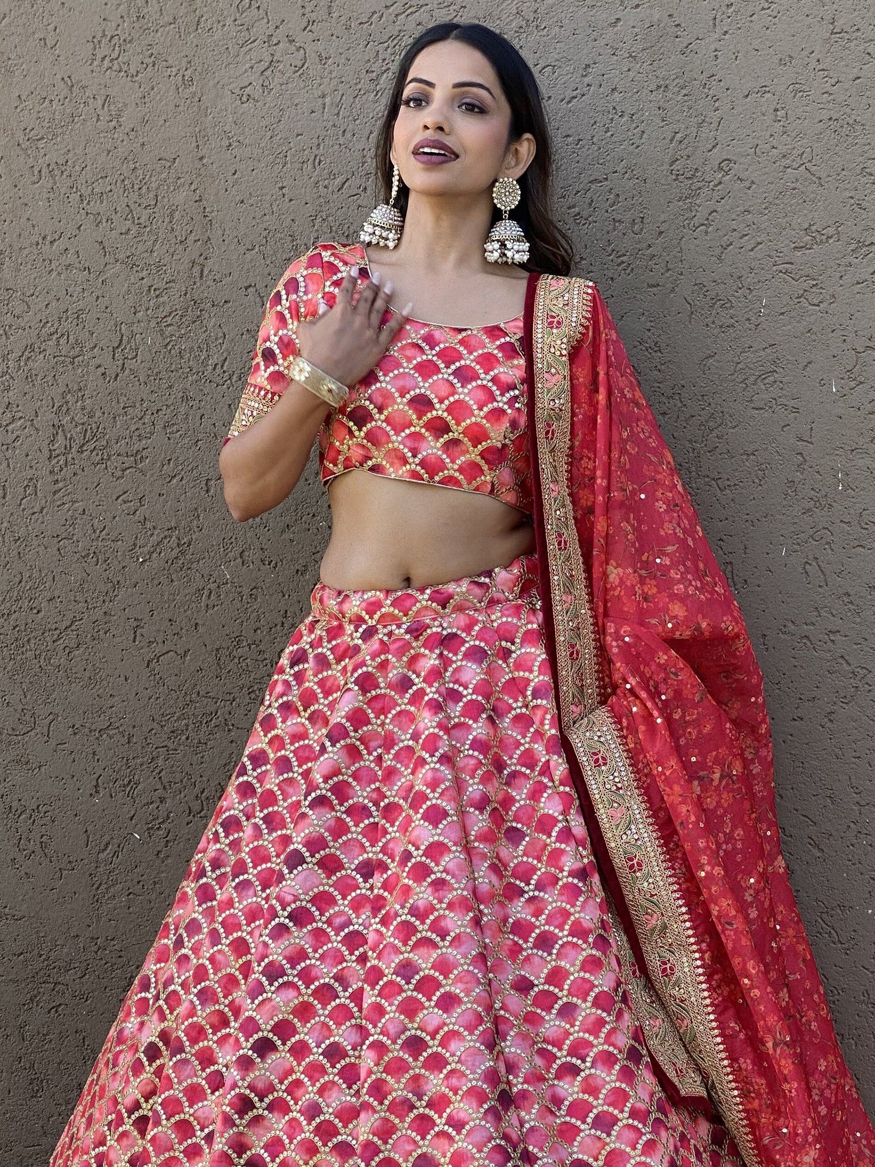 Red and pink designer lehenga choli with gold embroidery and floral dupatta, perfect for Indian weddings or festivals.