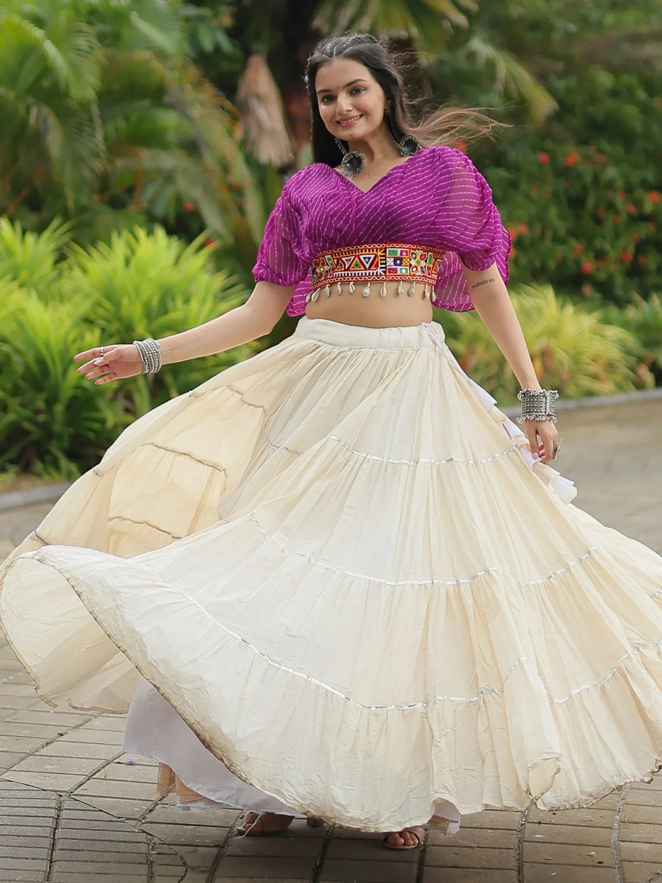 Woman in purple embroidered crop top and cream tiered skirt, twirling outdoors