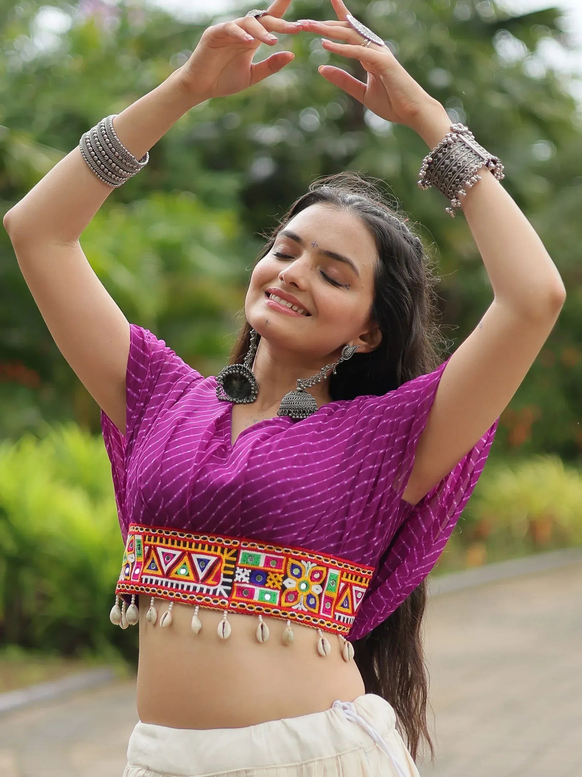 Woman in purple ethnic crop top with mirror work and shell trim, paired with white skirt and silver jewelry