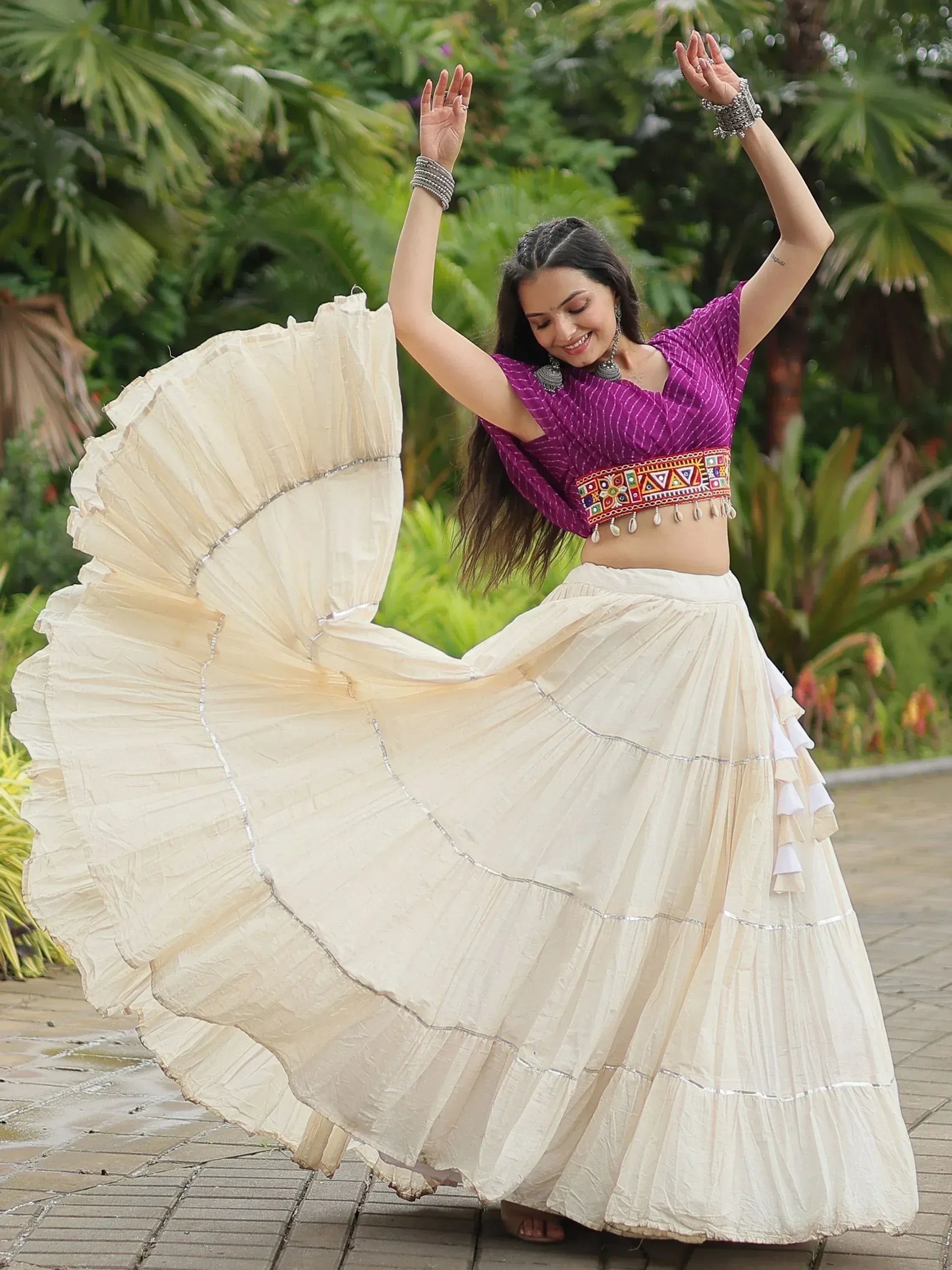 Woman dancing in purple embroidered crop top and flowing cream skirt, Indian ethnic wear