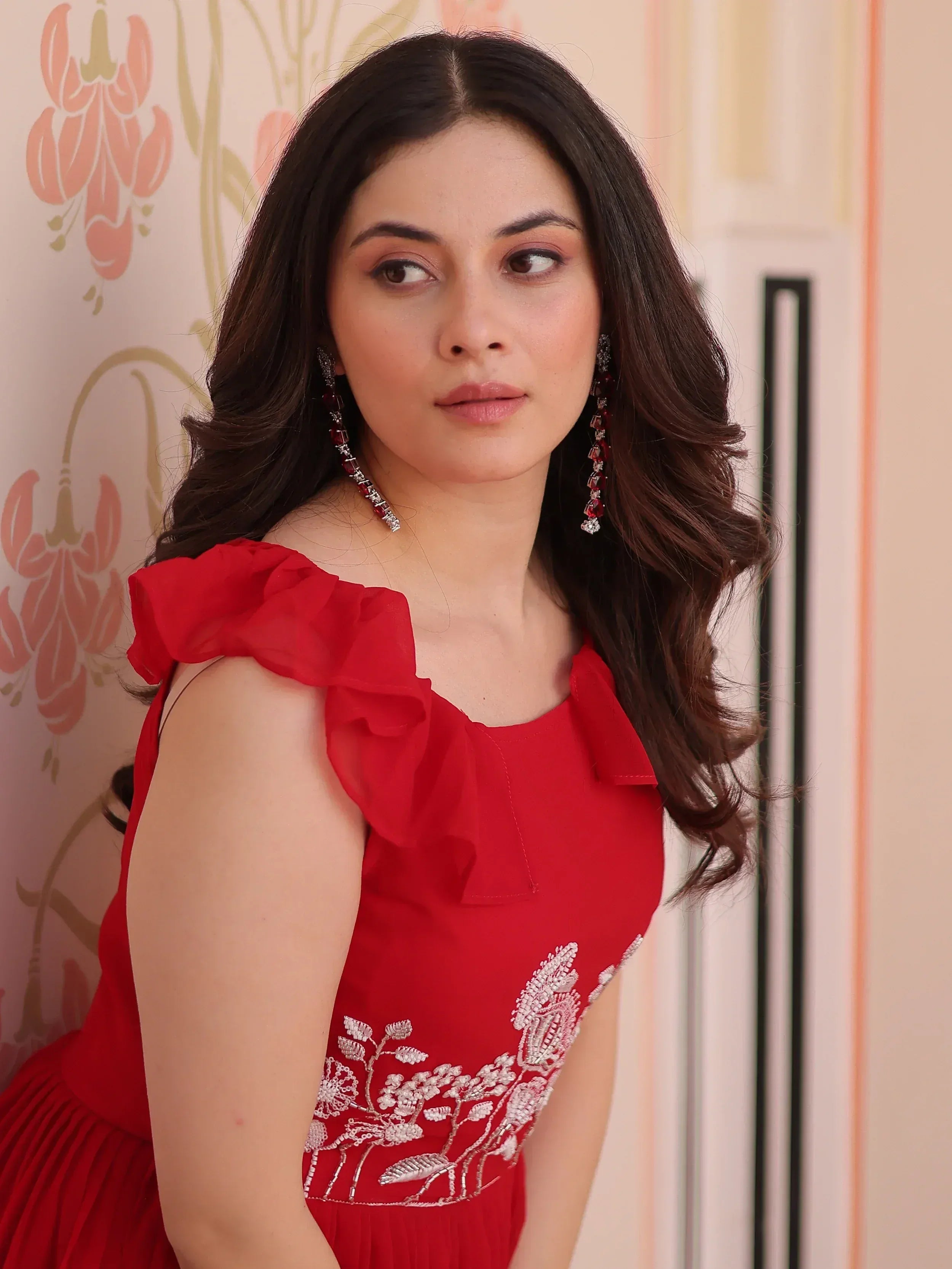 Red ethnic gown with floral embroidery and ruffled sleeves, paired with statement earrings.