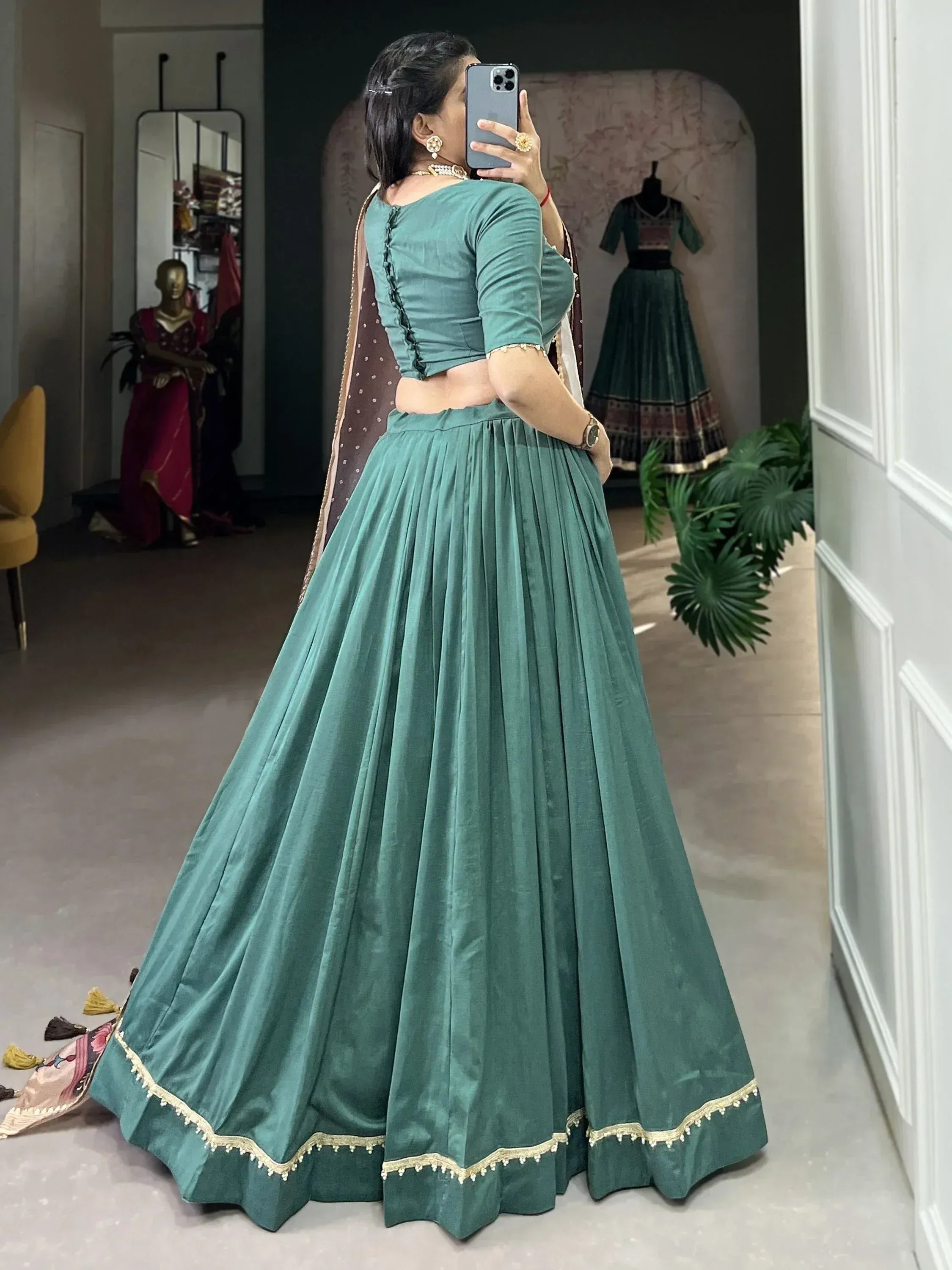 Teal velvet lehenga choli with gold trim, back view in boutique setting