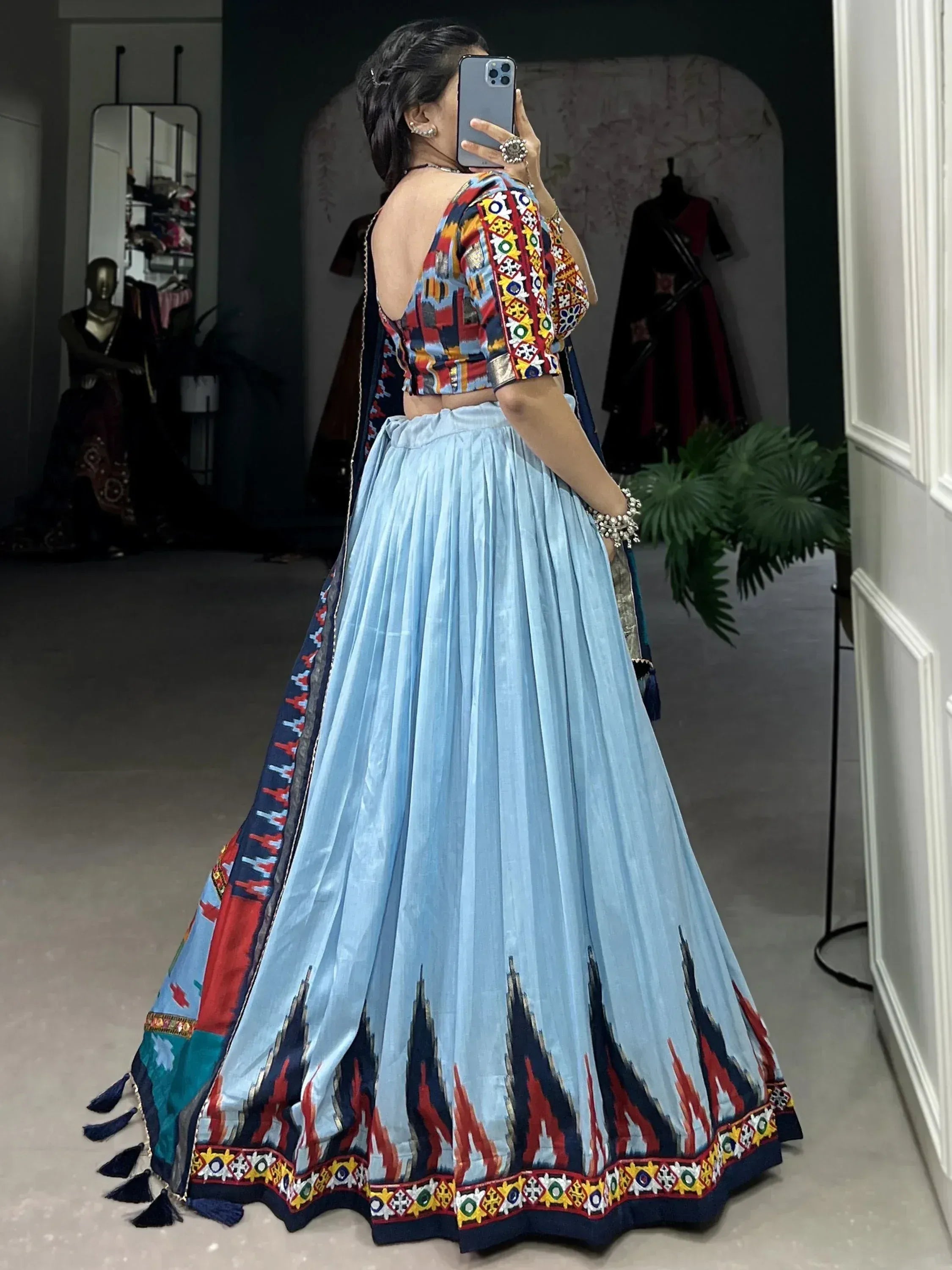 Woman in colorful embroidered lehenga choli with blue skirt, mirror selfie in boutique