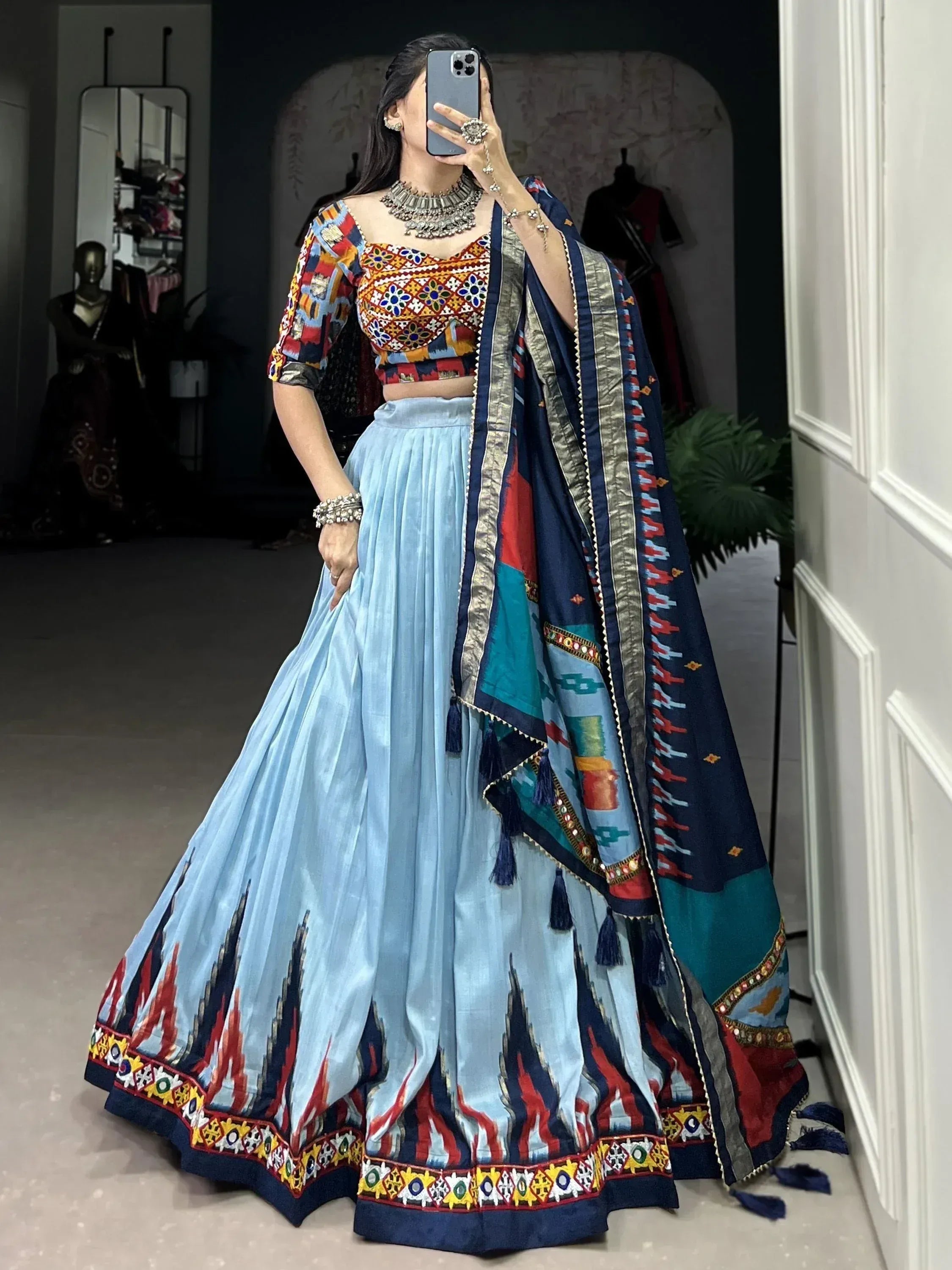 Woman in colorful embroidered lehenga choli with blue skirt and patterned dupatta, taking mirror selfie