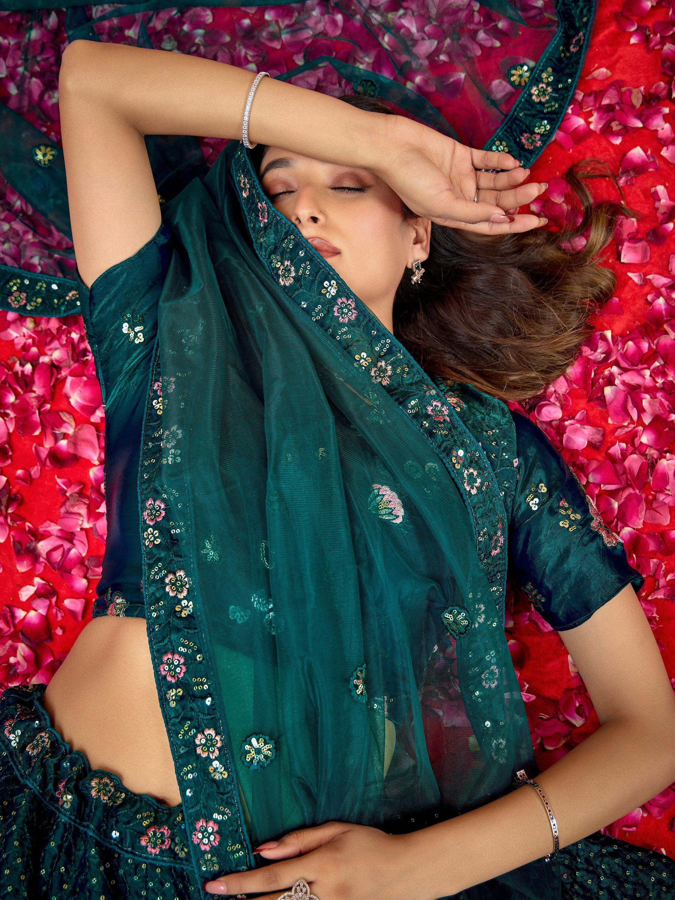 Woman in emerald green embroidered saree with floral sequins, lying on rose petals, ethnic wear