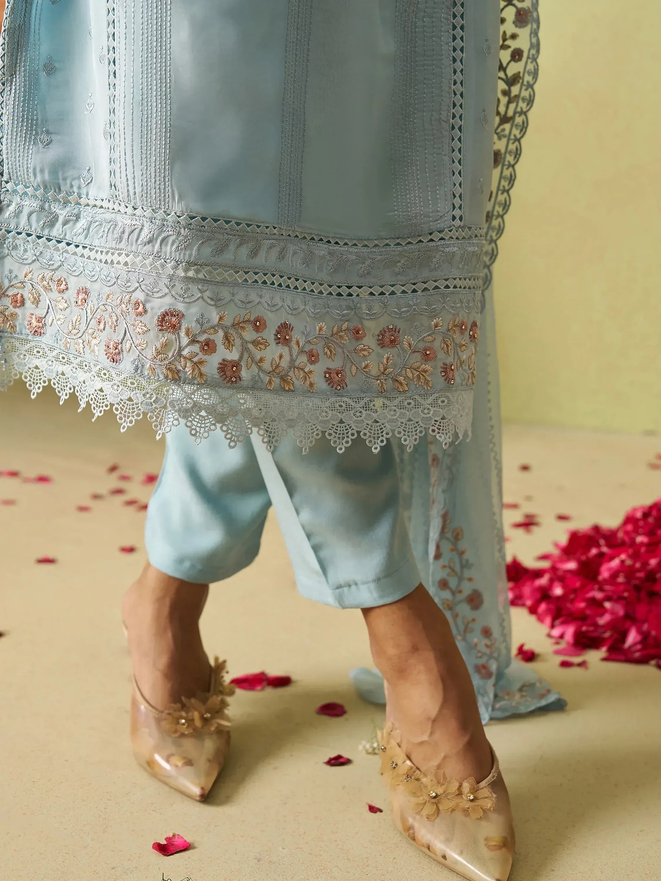 Light blue embroidered salwar kameez with floral lace hem and matching heels, rose petals scattered