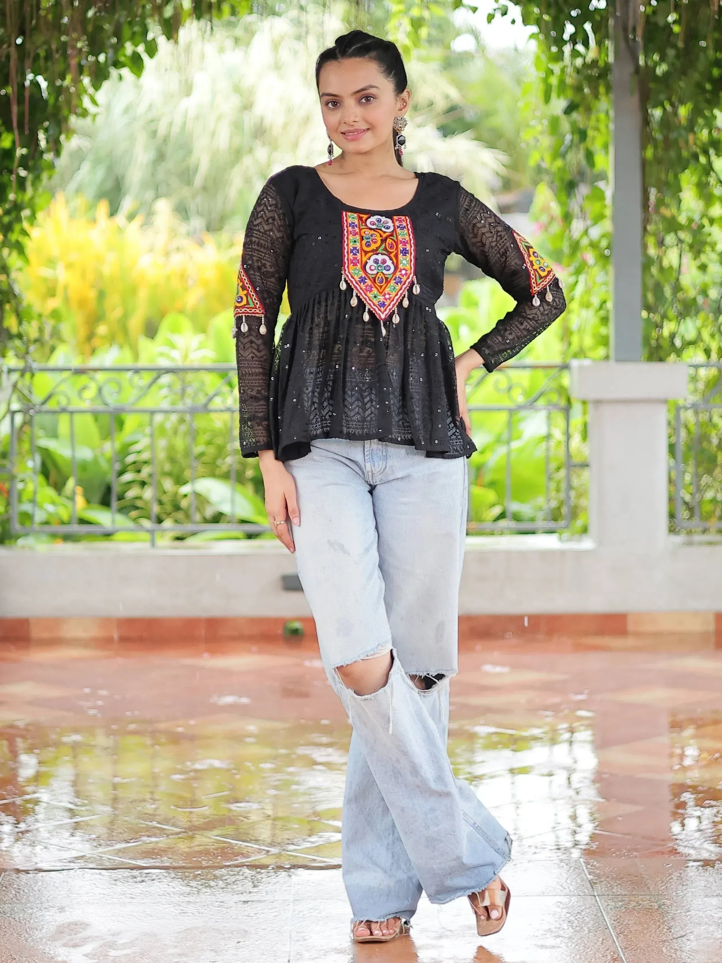 Black embroidered top with colorful patterns paired with ripped jeans, styled for ethnic fashion.