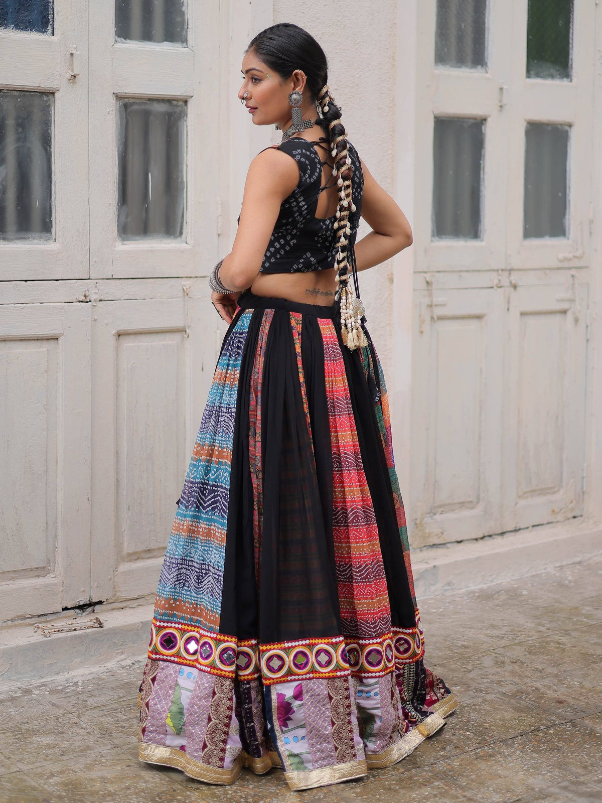 Woman in colorful Indian ethnic lehenga choli with mirror work, standing by white doors