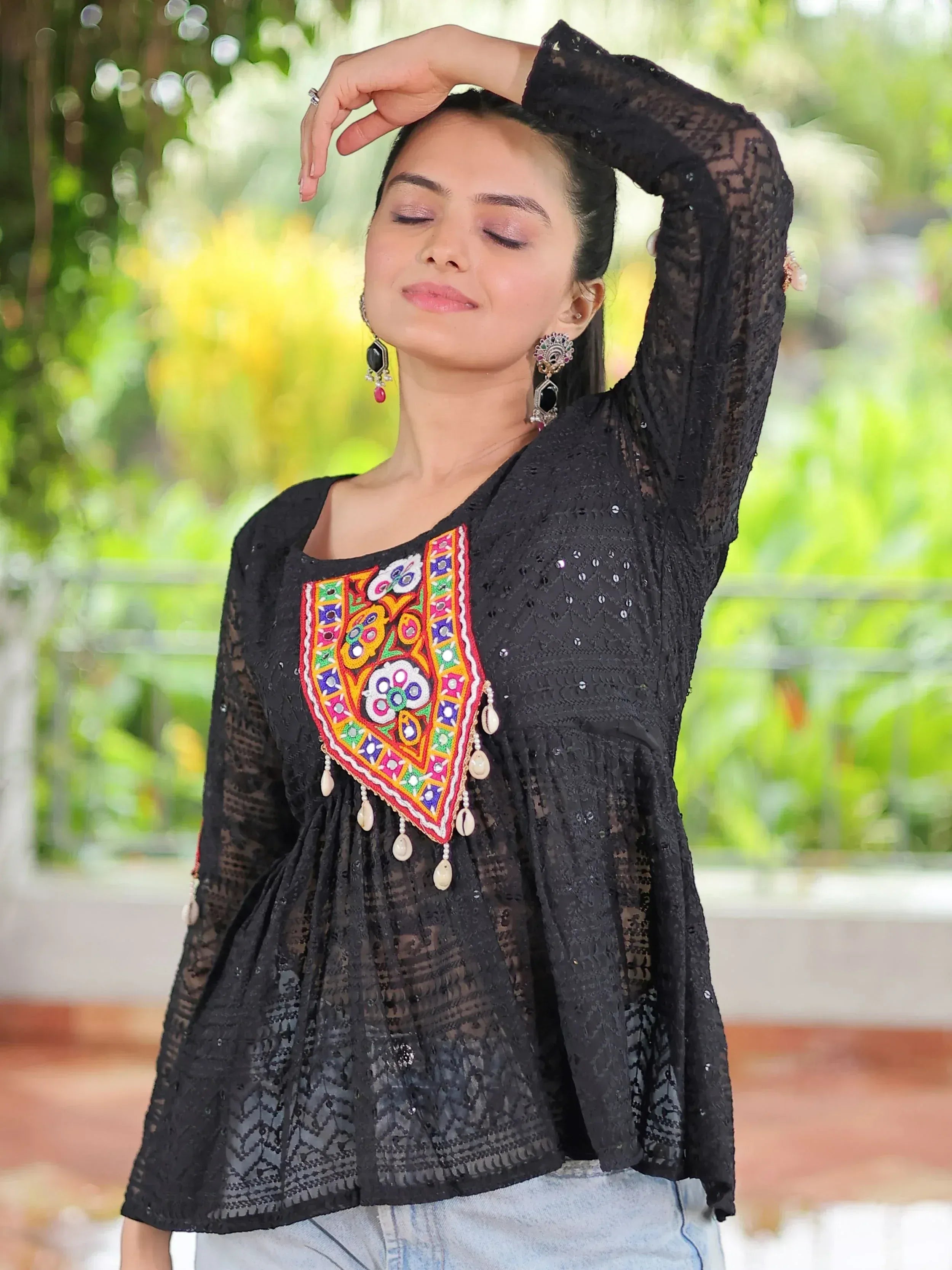 Black lace top with colorful embroidery and tassels, paired with jeans for a stylish ethnic look.