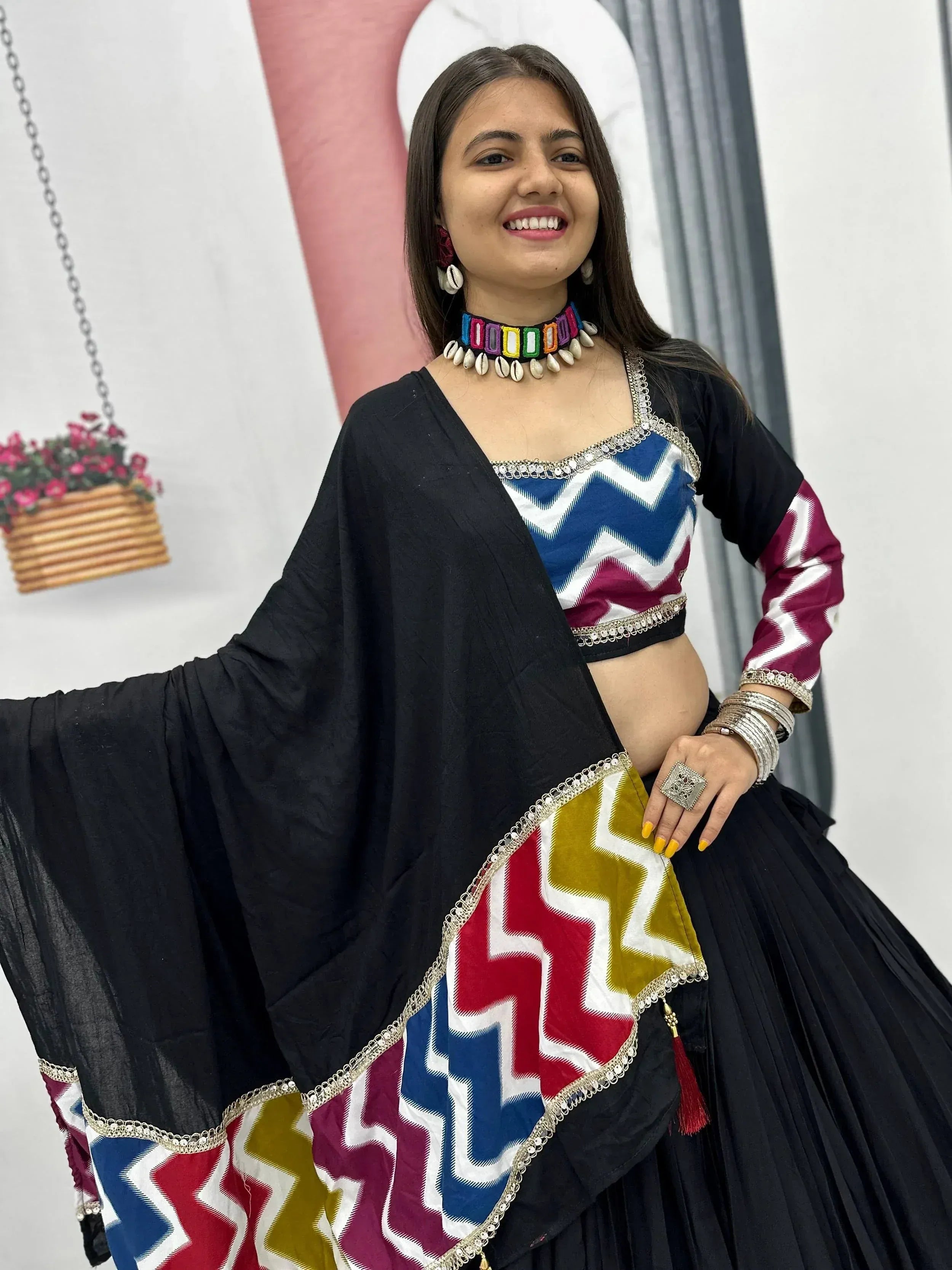 Woman in colorful ethnic lehenga choli with geometric print, black dupatta, and traditional jewelry