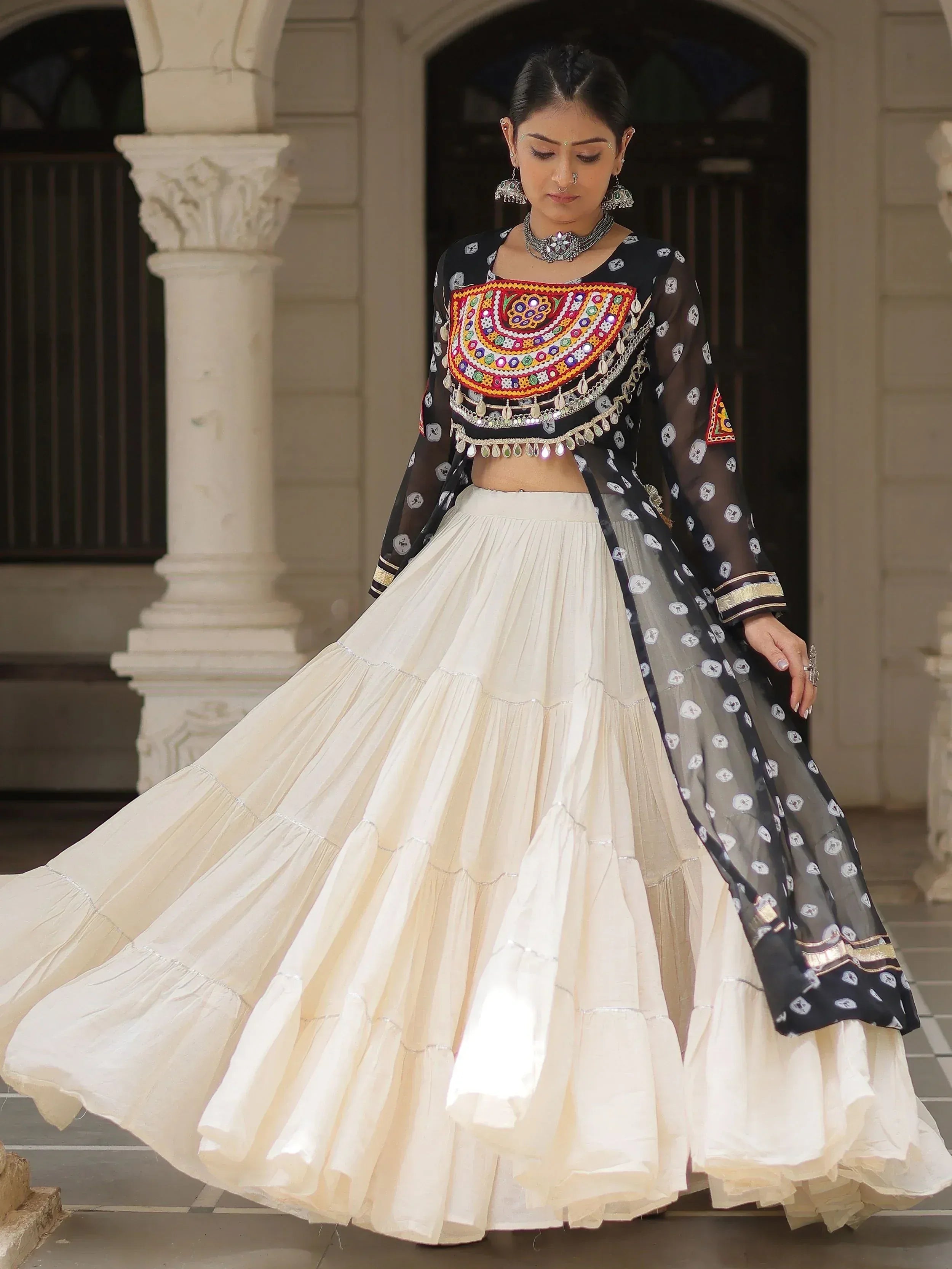 Woman in black embroidered crop top with cream tiered skirt, Indian ethnic wear, mirror work, traditional jewelry
