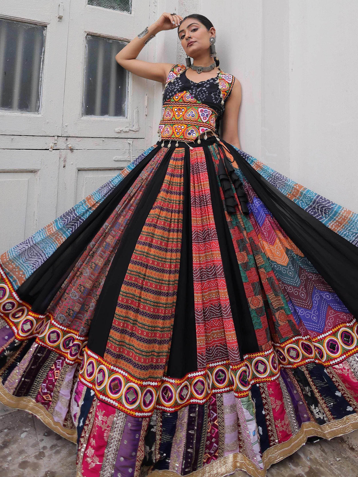Woman in vibrant Indian ethnic lehenga choli with mirror work, colorful patchwork skirt, and traditional jewelry.
