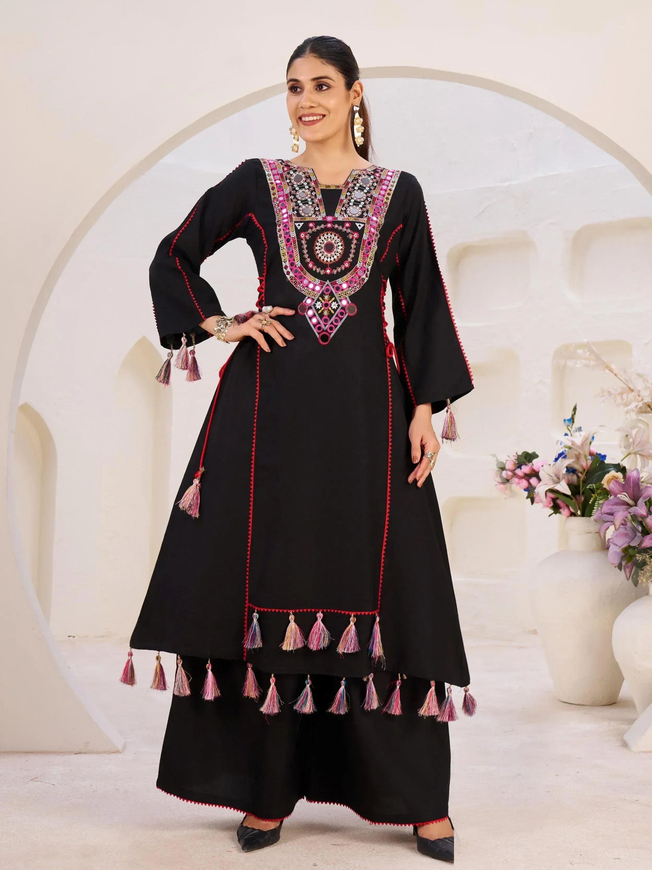 Black ethnic kurti with mirror work, pink embroidery, and tassels, paired with palazzo pants for festive occasions