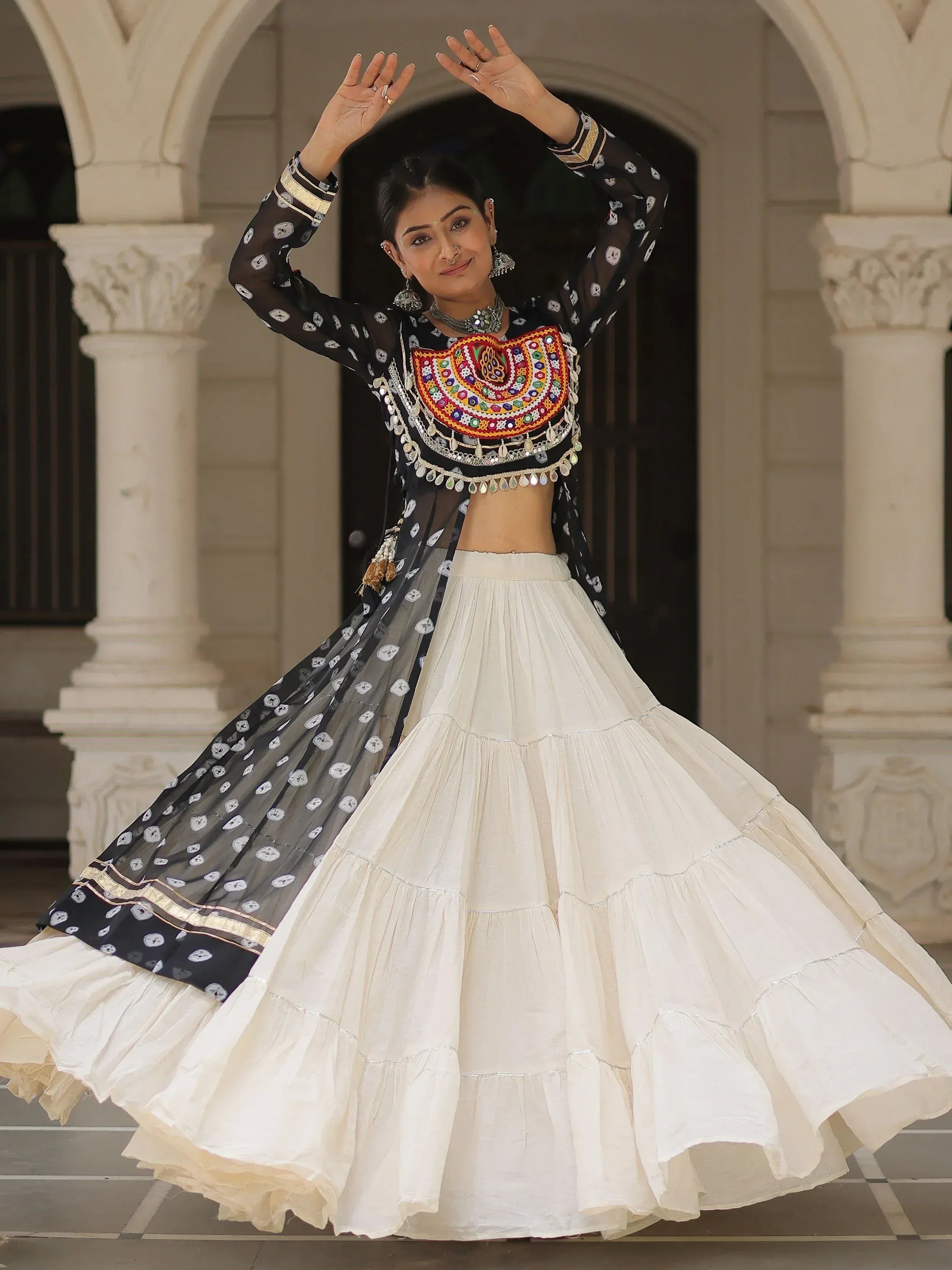 Woman in black and white ethnic lehenga choli with mirror work, dancing under arches