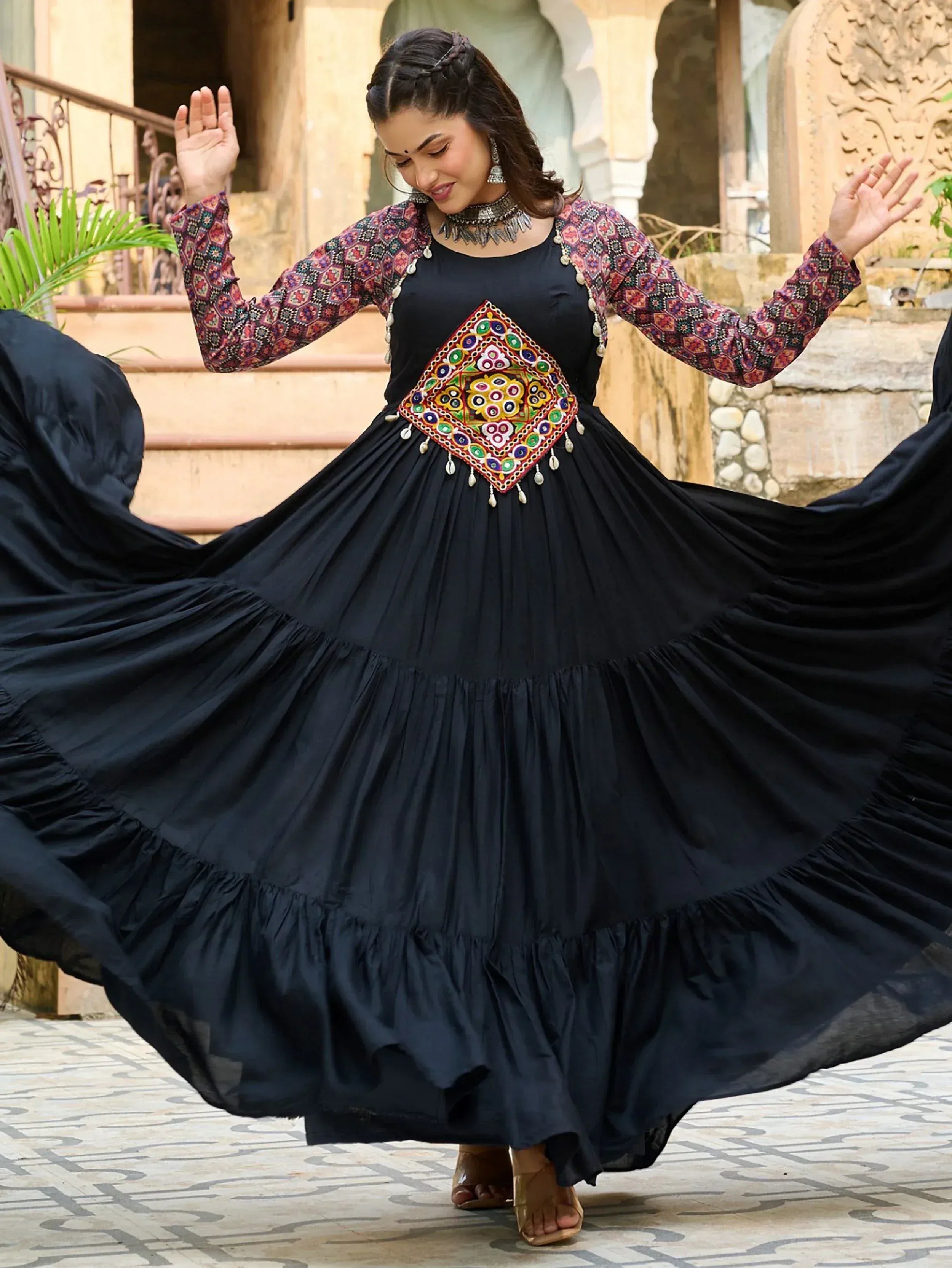 Woman twirling in black ethnic gown with colorful embroidery and tiered skirt, perfect for Indian festive occasions.