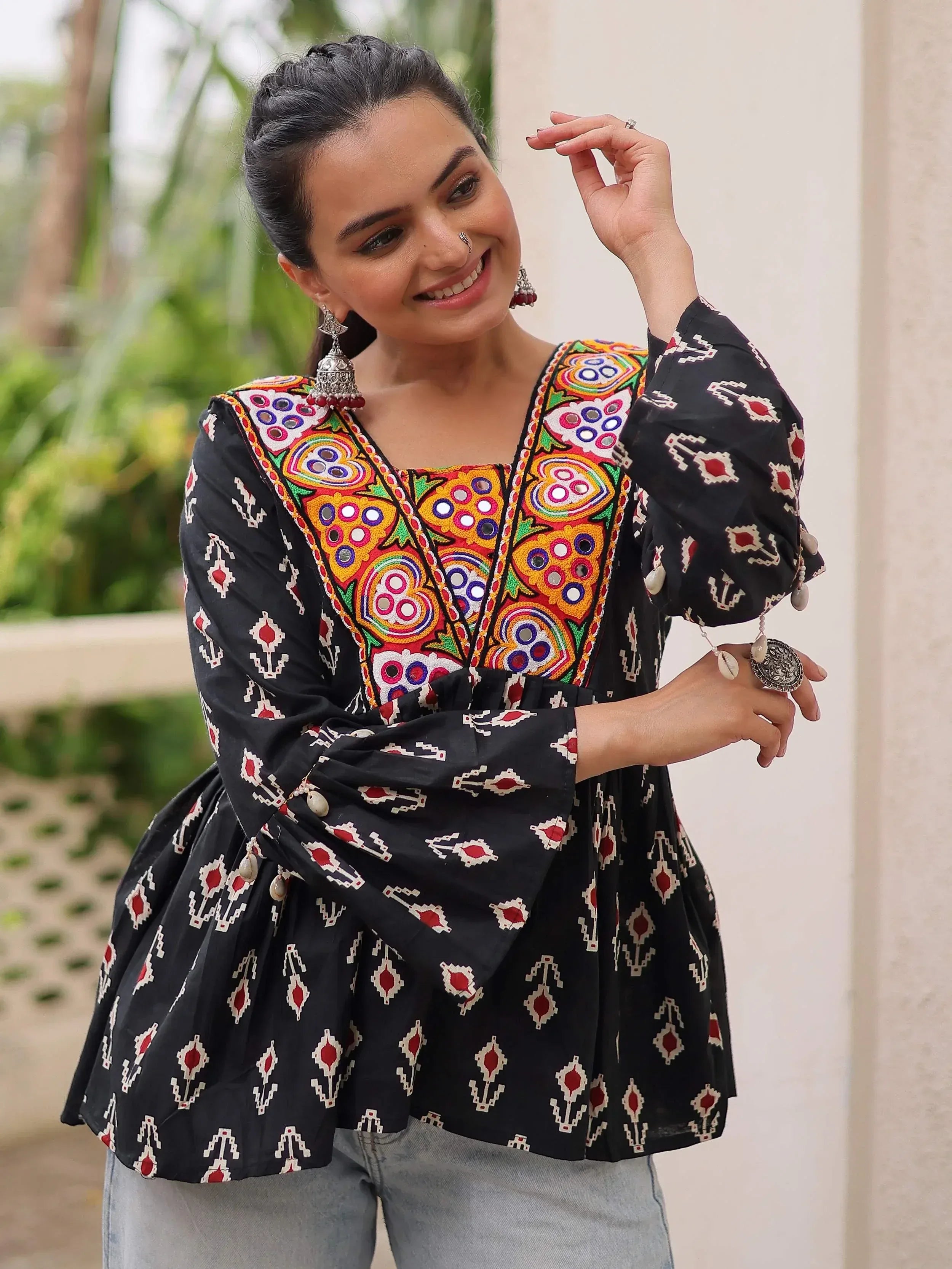 Black ethnic top with colorful mirror embroidery and geometric print, paired with jeans for casual wear.