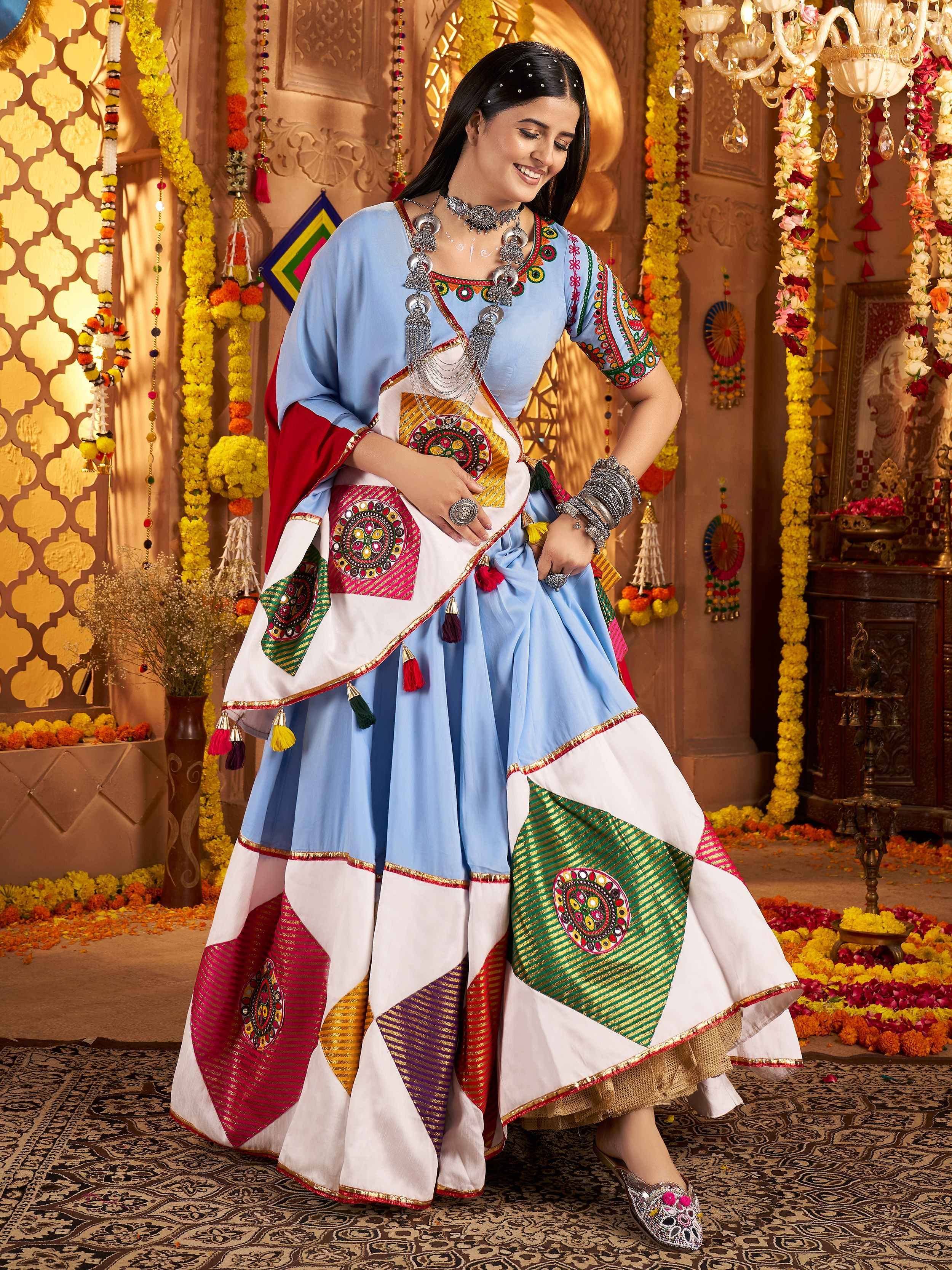 Woman in vibrant blue and white embroidered ethnic sharara set with mirror work, perfect for festive occasions.